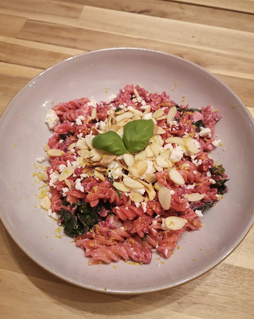 A pink pasta dish with flaked almonds and some basil leaves