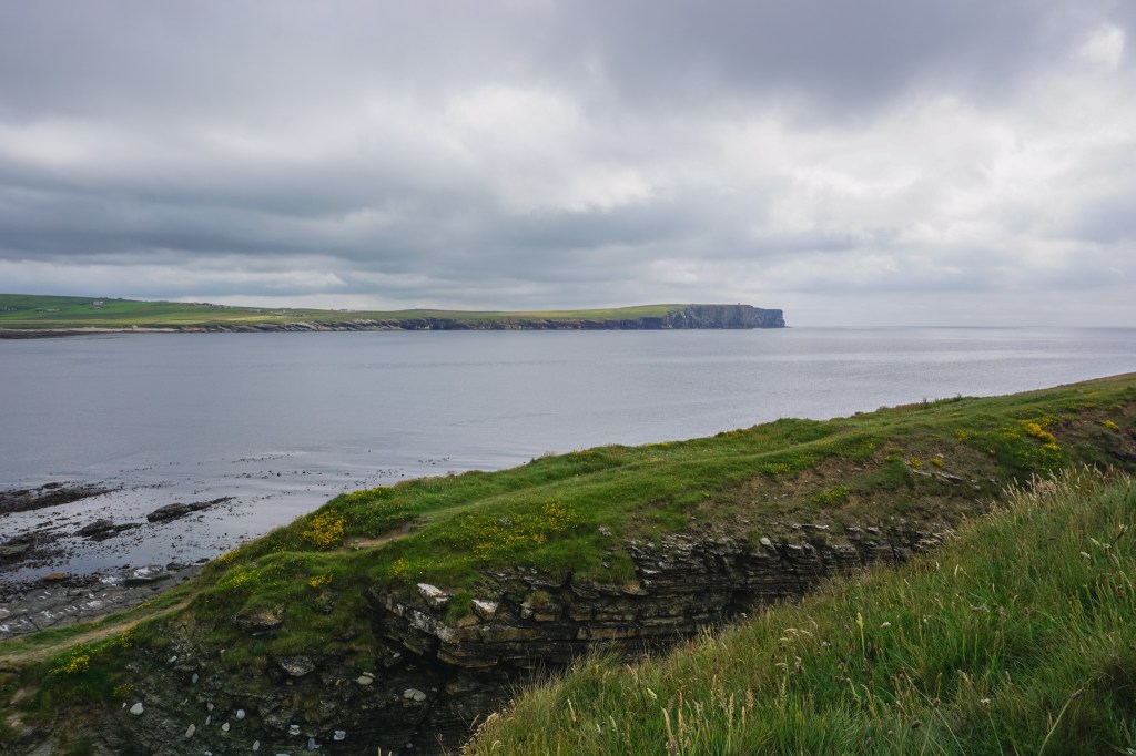 There are green hills and cliffs either side of the sea