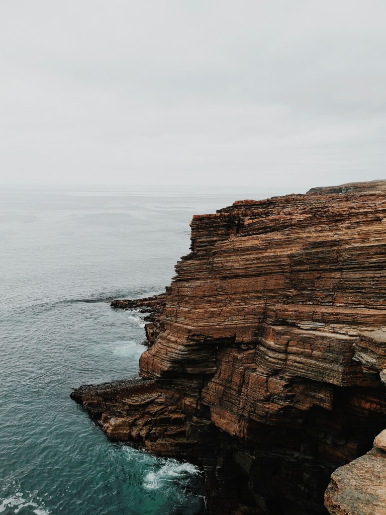 A layered brown cliffside poking out into the sea