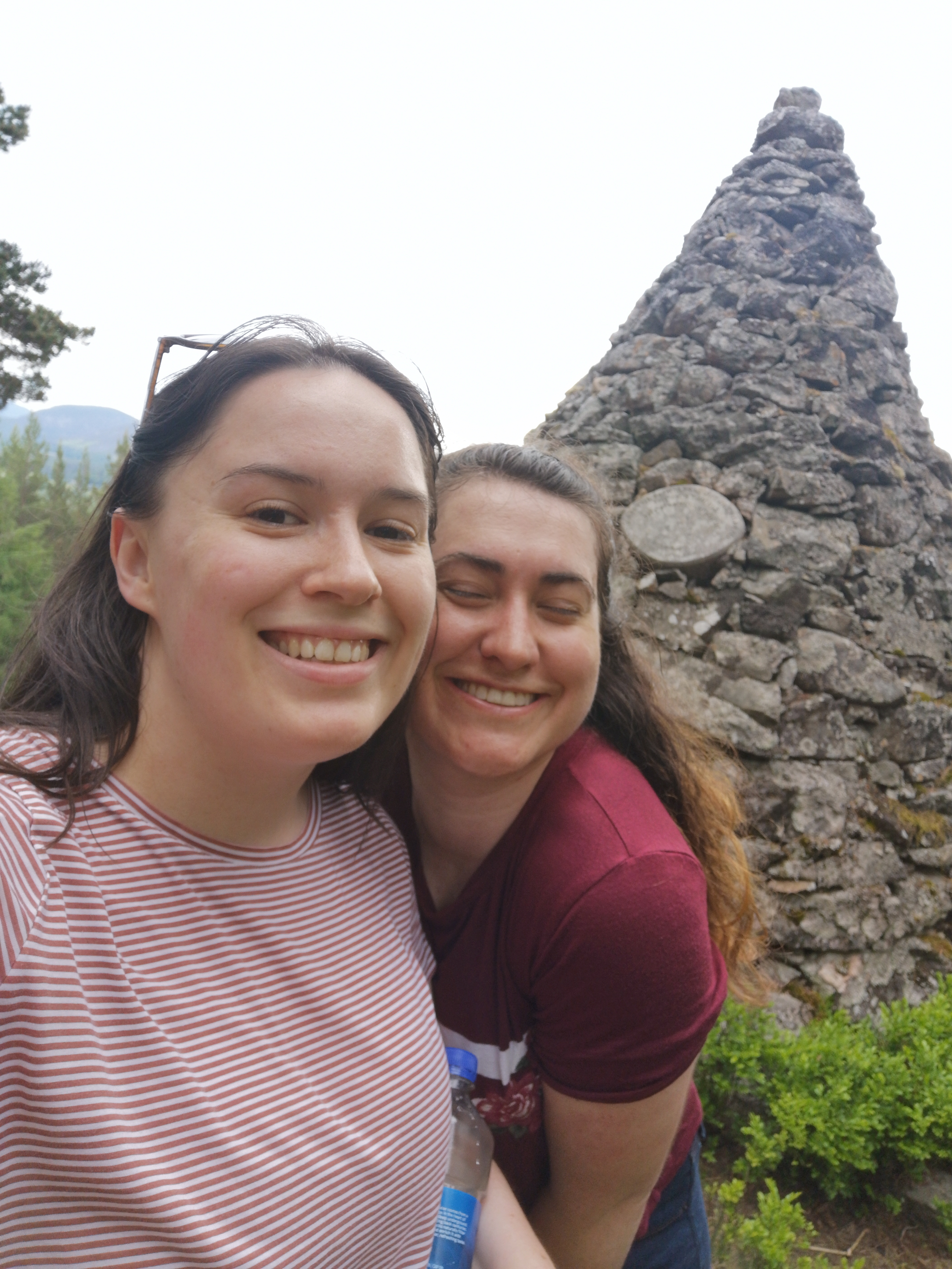 Two women smile with their faces pressed together, there is a pyramid made our grey rocks behind them