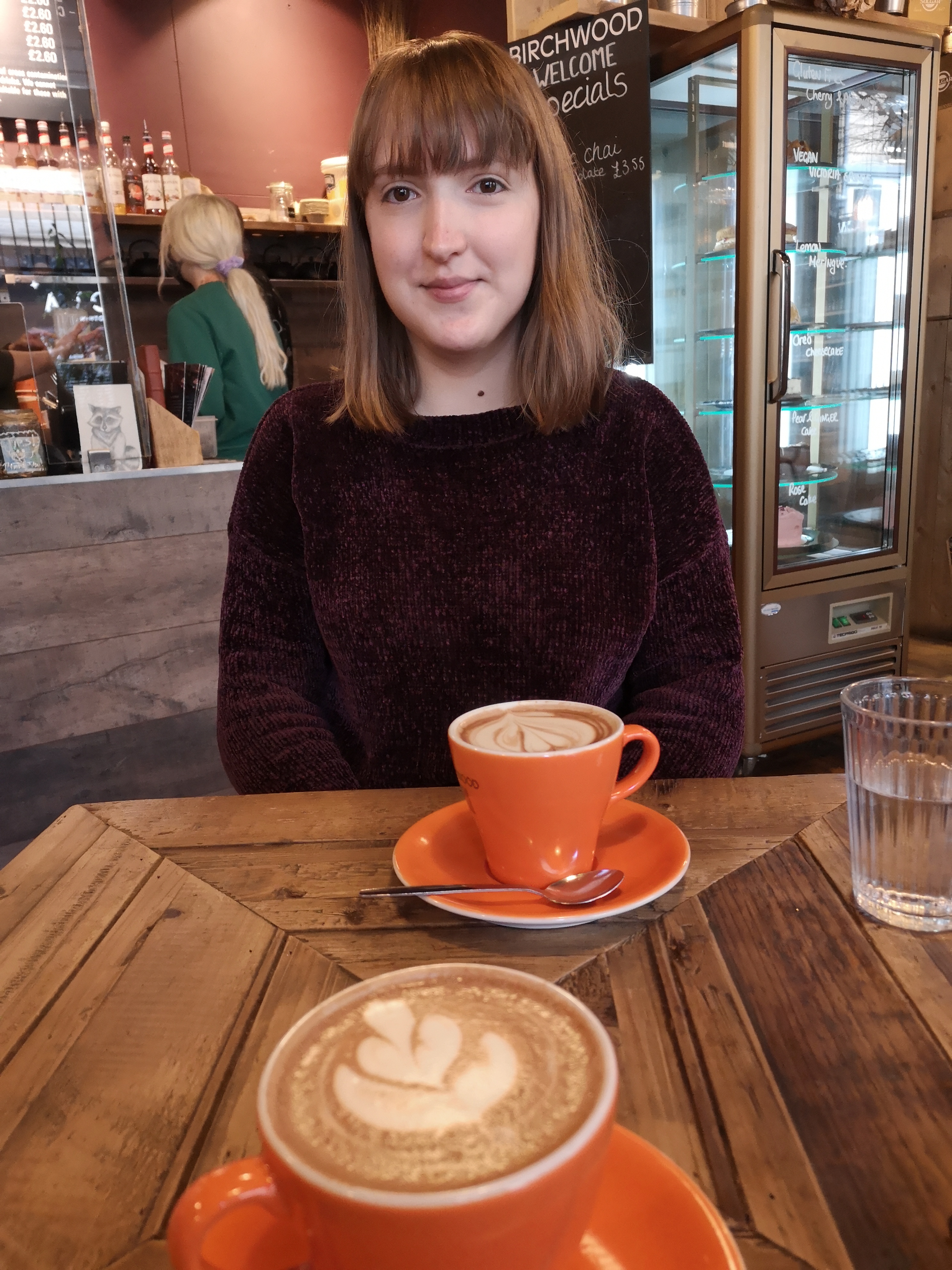 A woman smiles at a table with two coffees on it