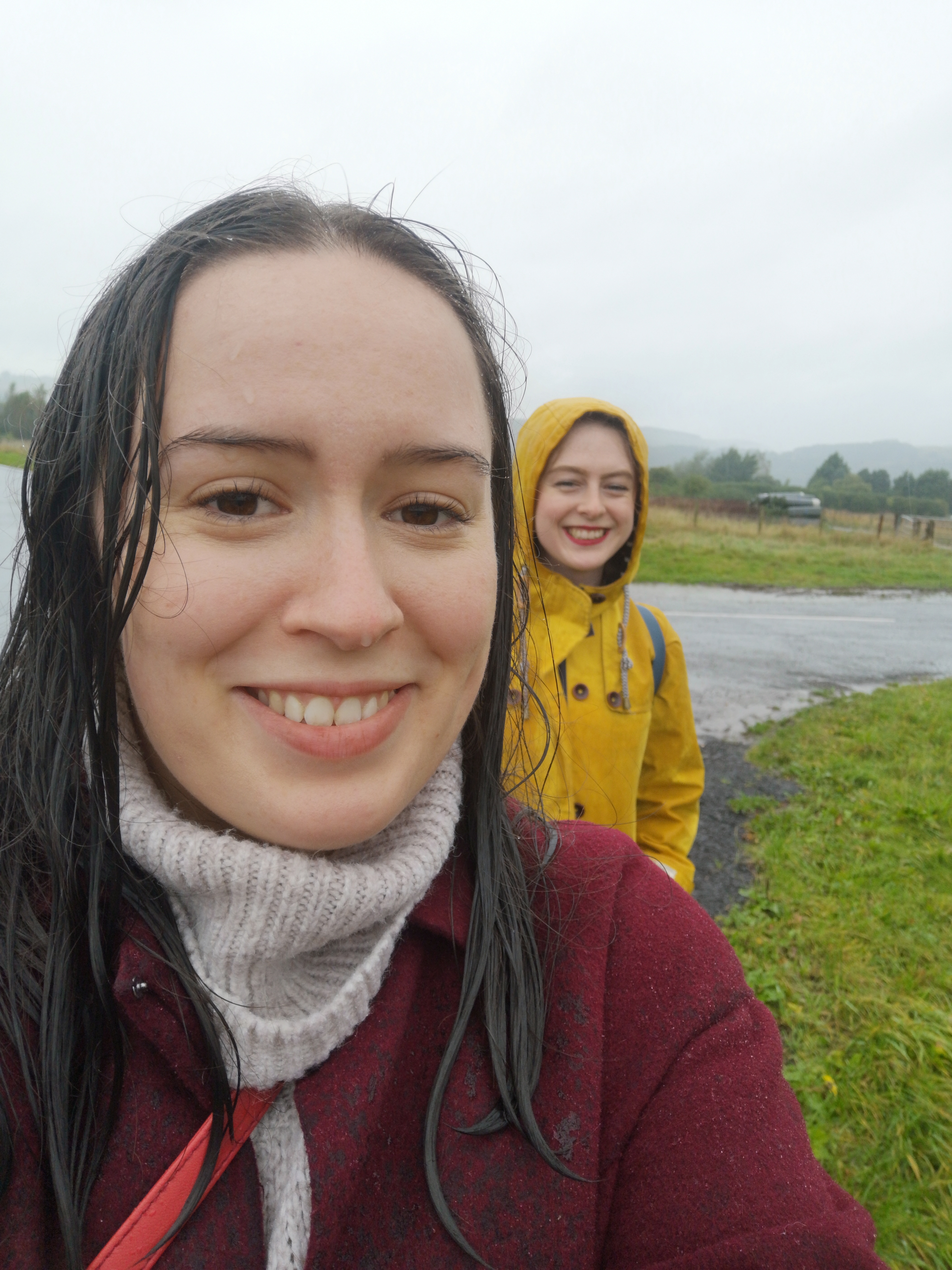 Two women smile despite being drenched in the rain