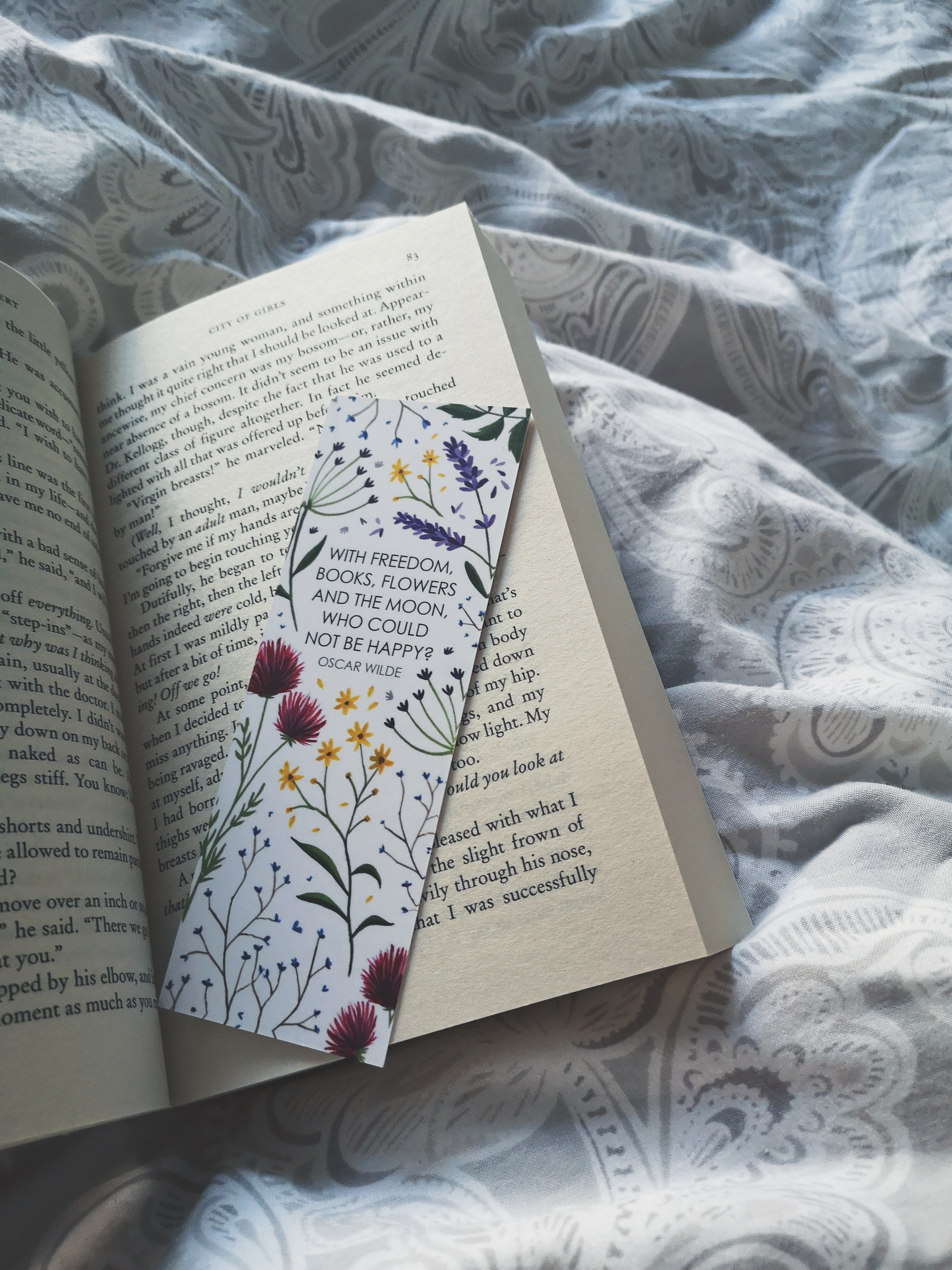 An open book on top of bedsheets, there is a floral bookmark inside