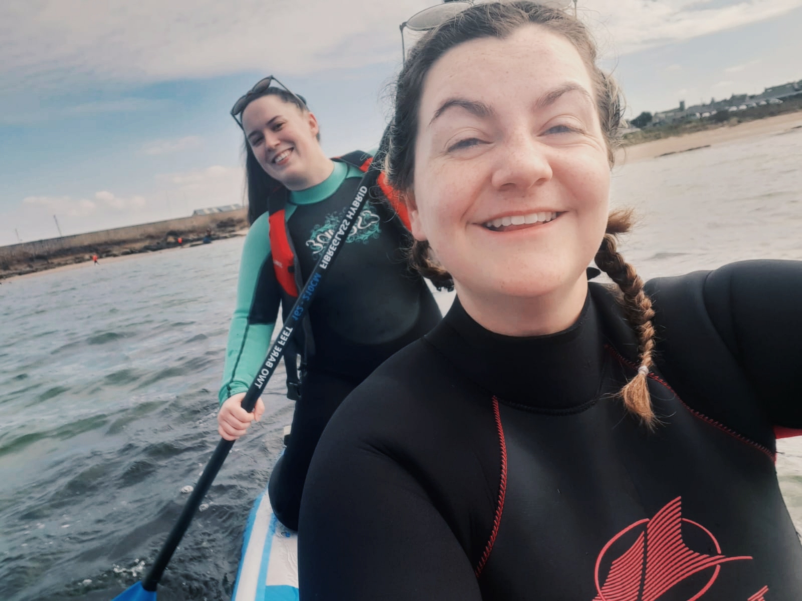 Two women smile as they sit and kneel on a paddle board together