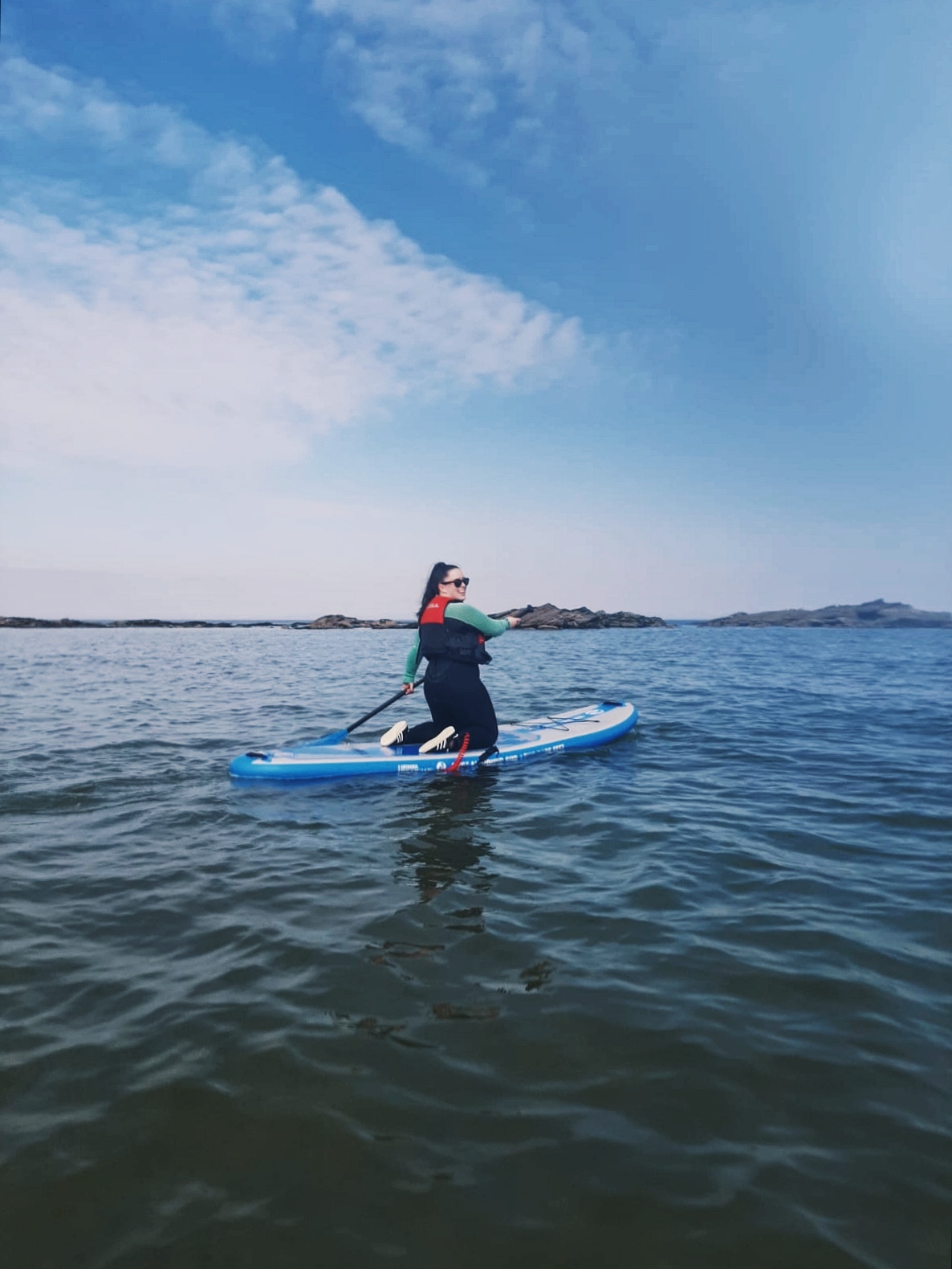 A woman kneels on a paddle board in the sea