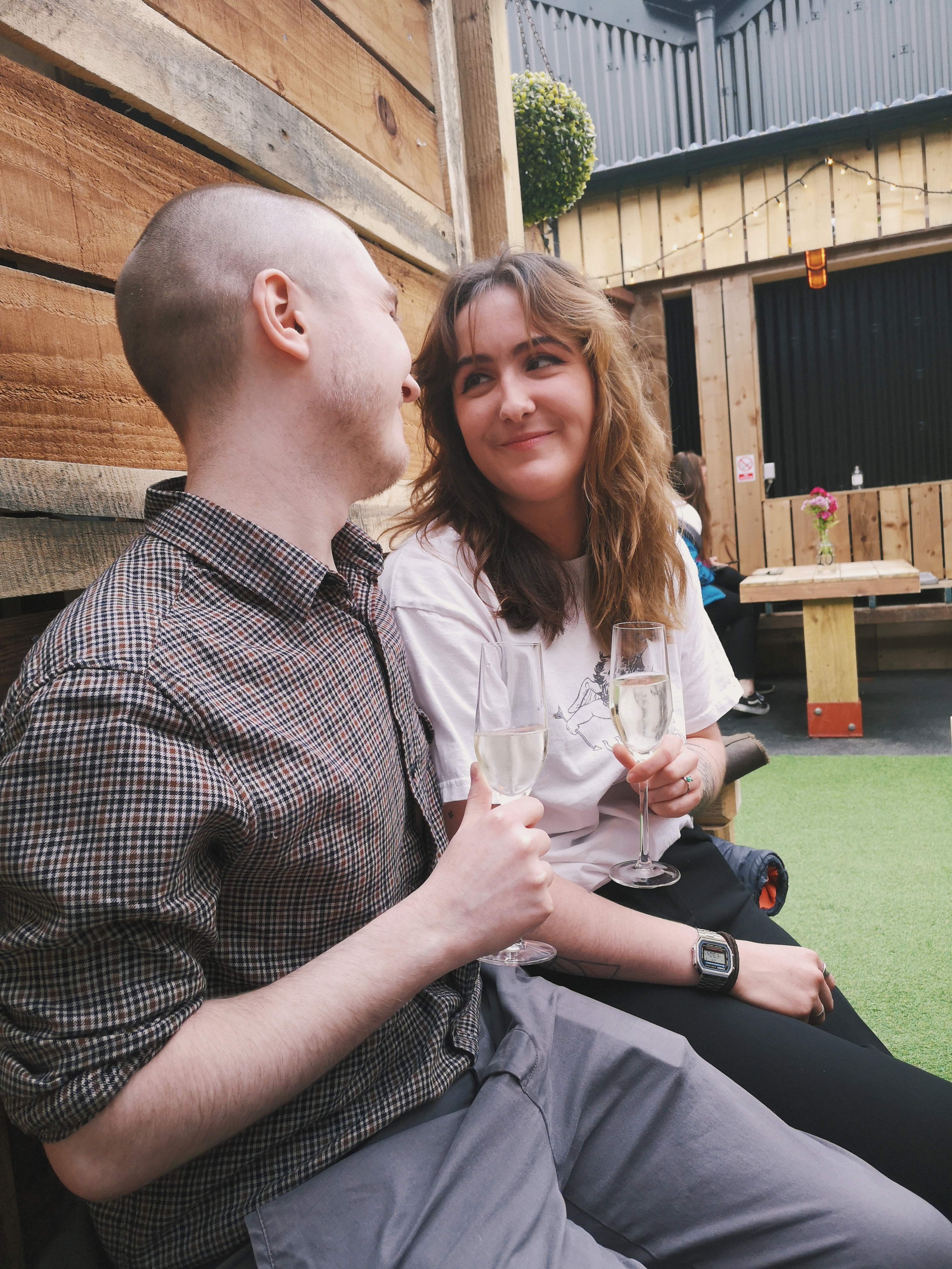 A couple look at each other, smiling, as they hold flutes full of champagne