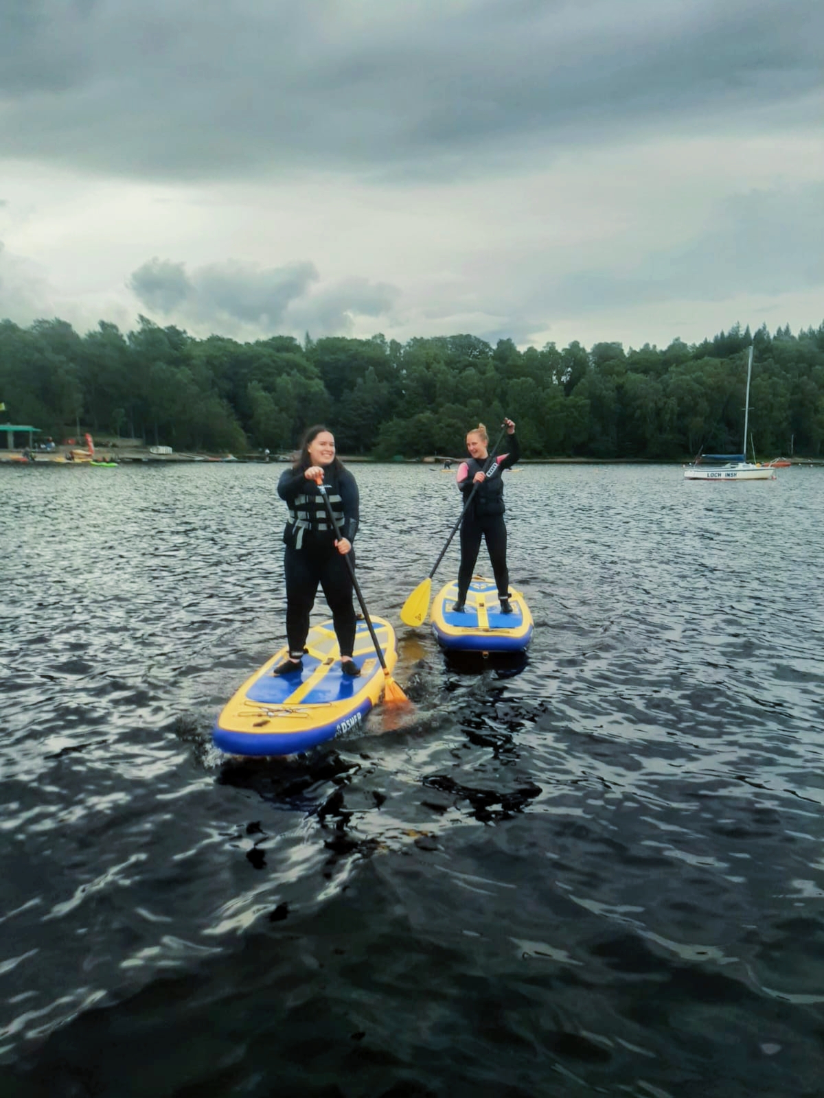 Two women stand on paddle boards in a loch