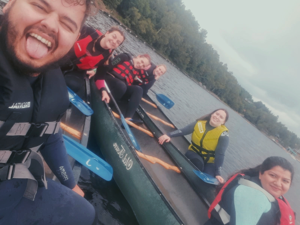 Six people smile while sat in canoes on a loch