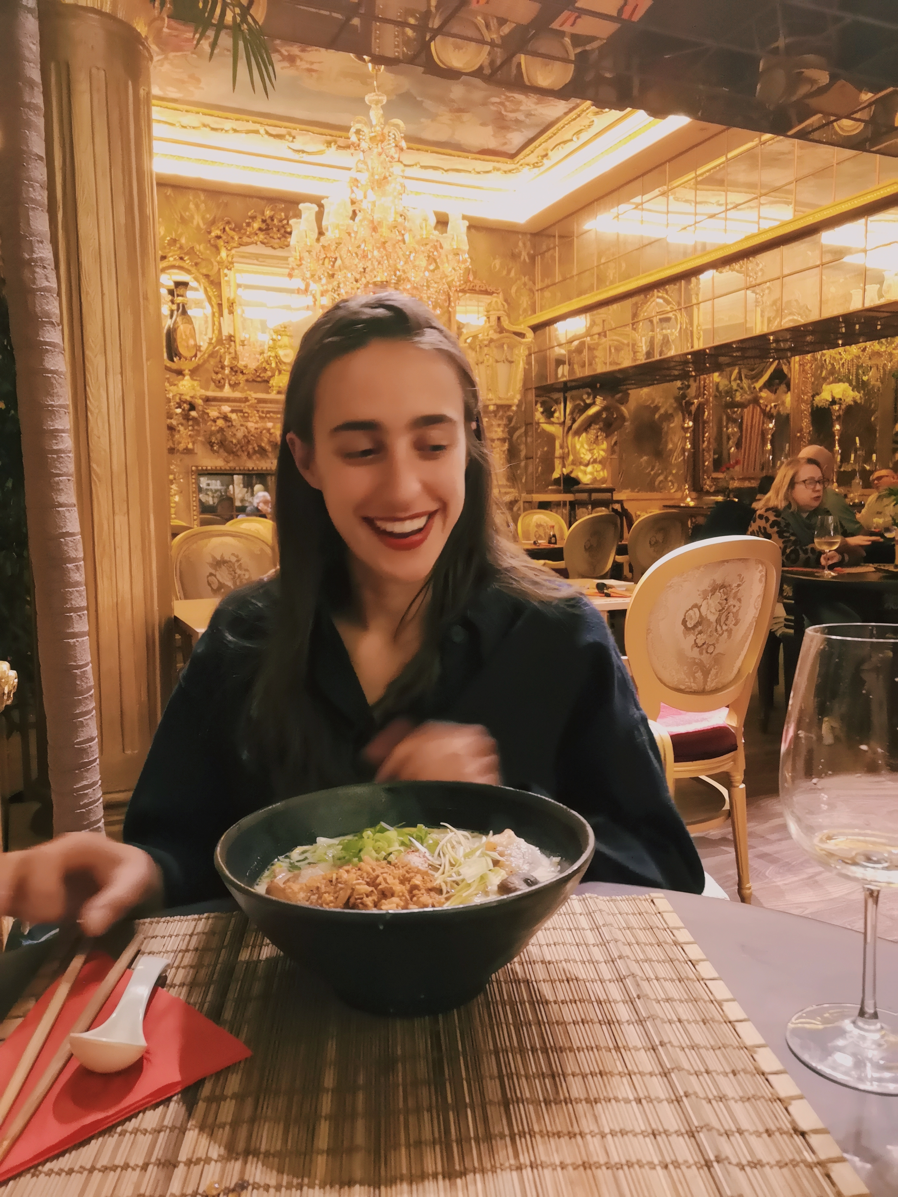 A woman smiles while looking down at a big bowl of ramen