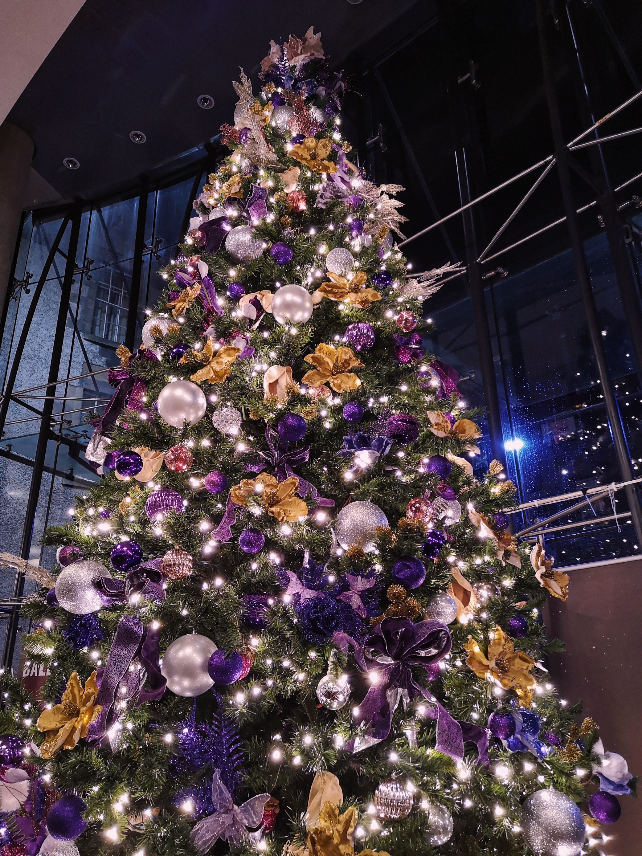 A big Christmas tree with purple and gold decorations, some of which are ballet pointe shoes