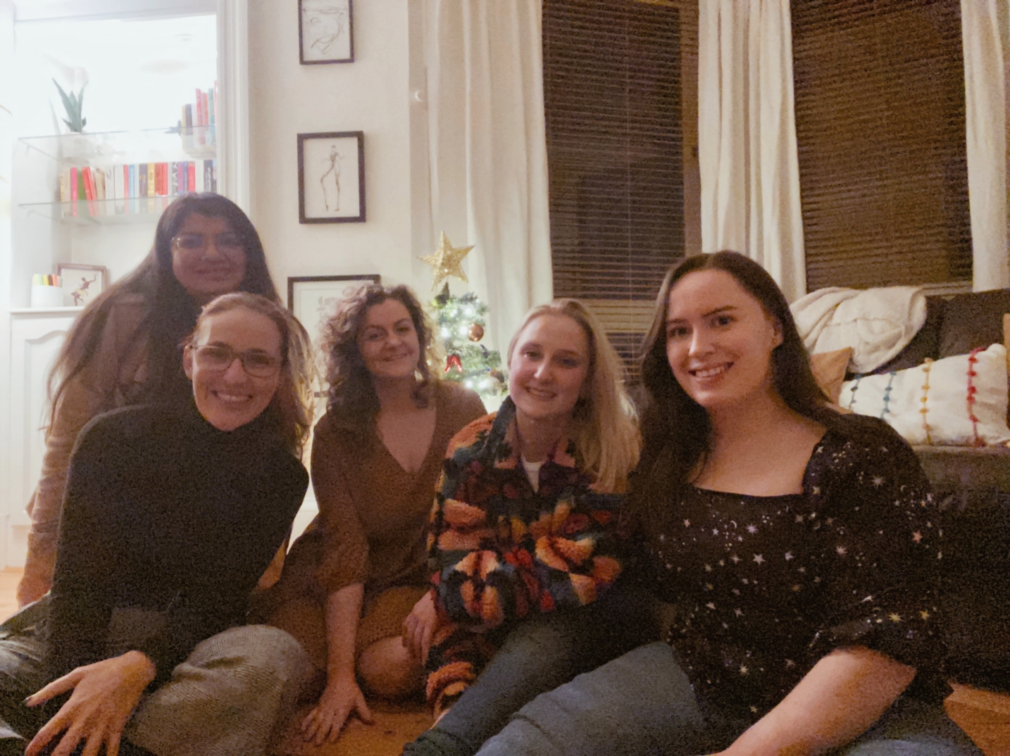 Five women sit in a living room and smile