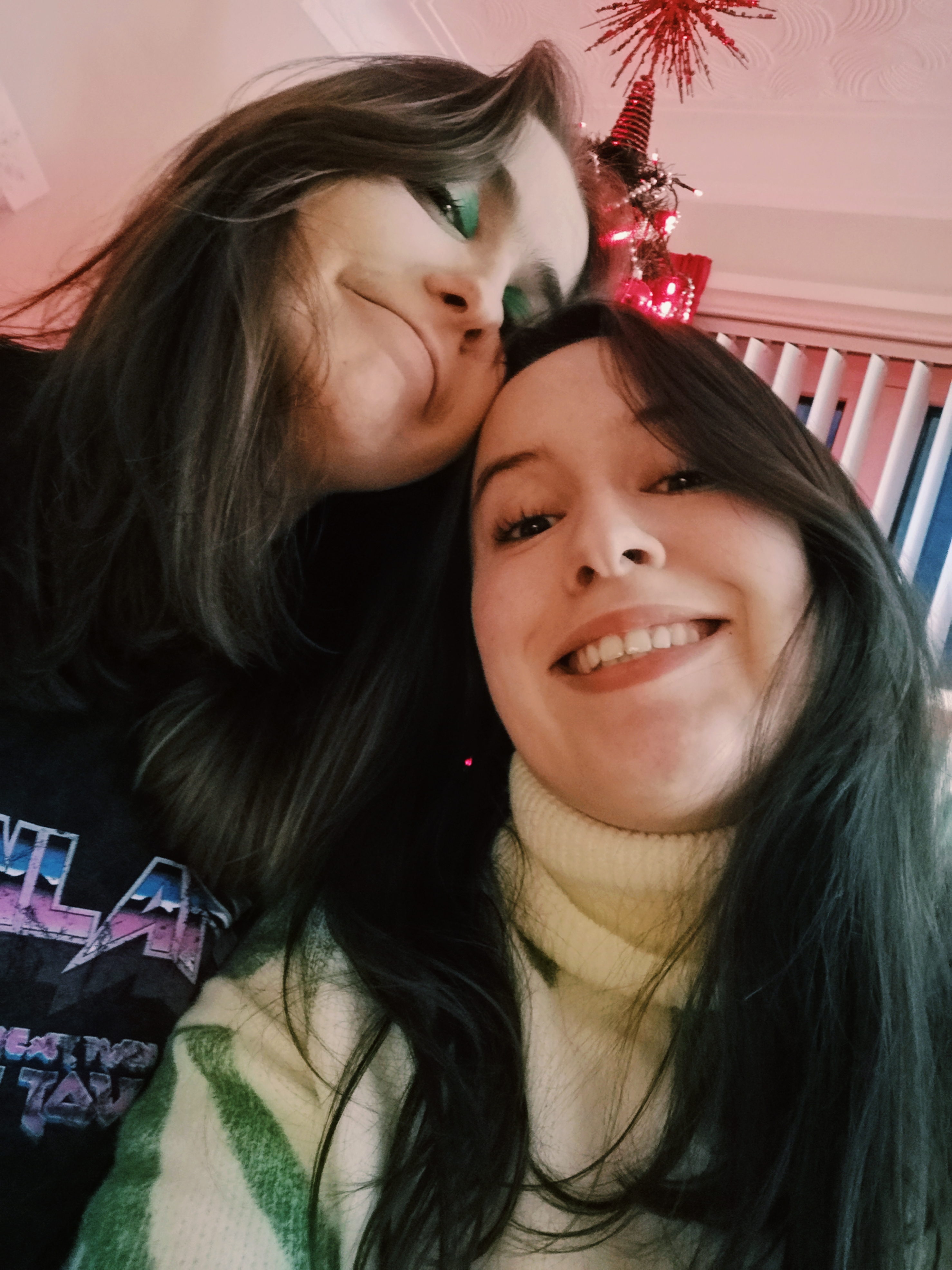 Two sisters look down at the camera smiling, leaning their heads together