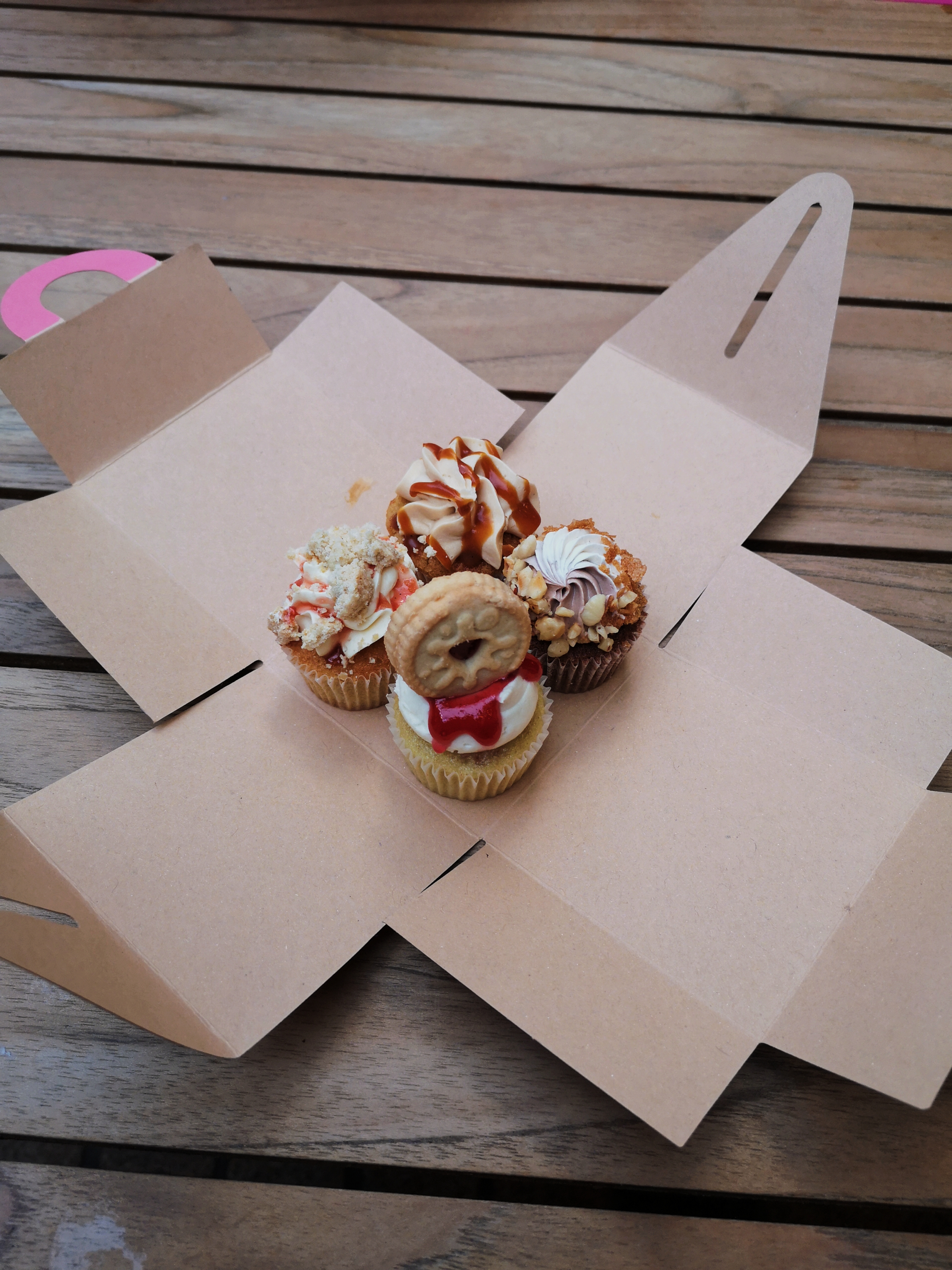 Four tiny cupcakes sit in the middle of a folded out box, one has a wee jammy dodger biscuit on top