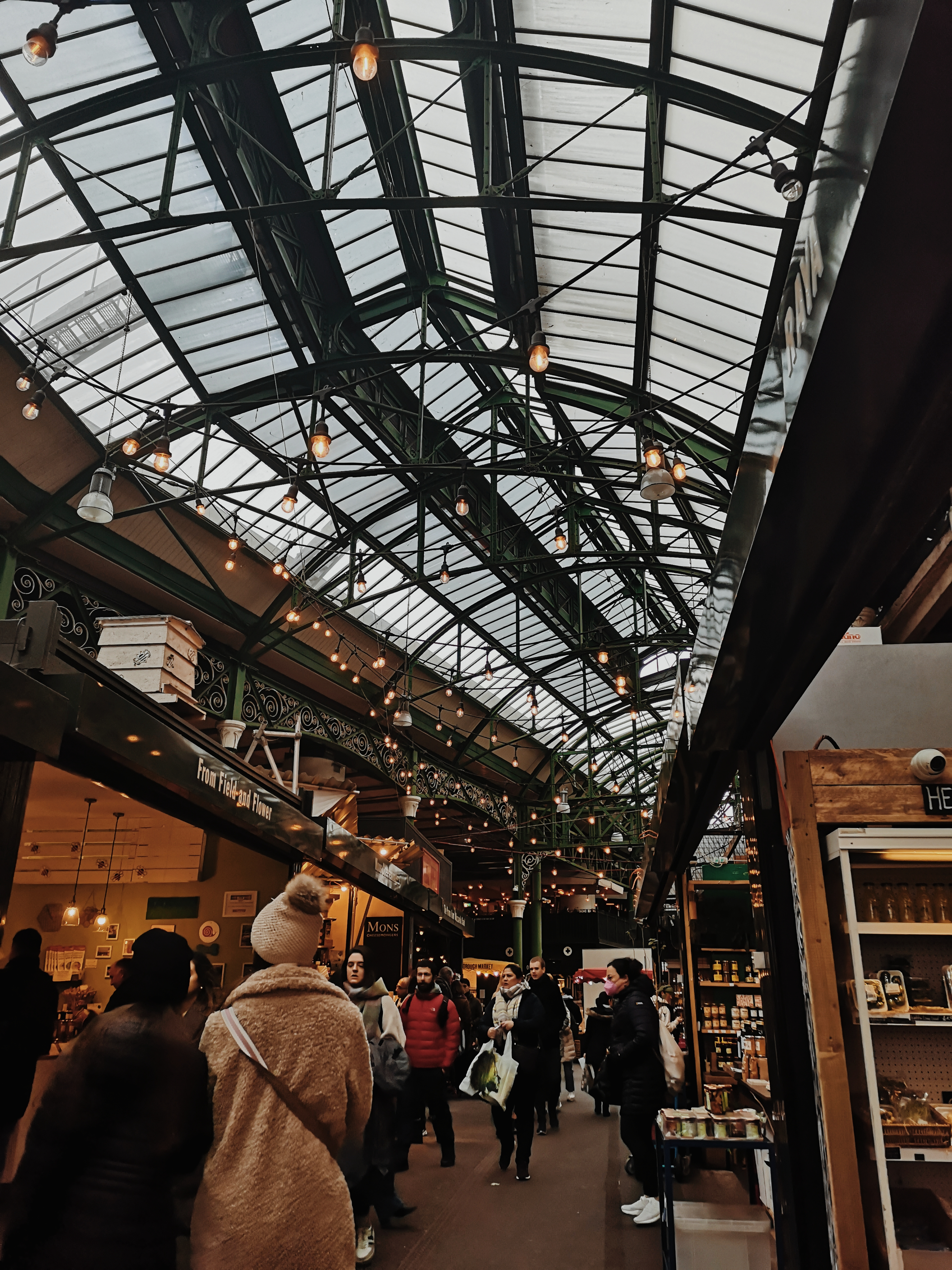 Market stalls line a path and the green frame of the roof and strung with hanging lightbulbs