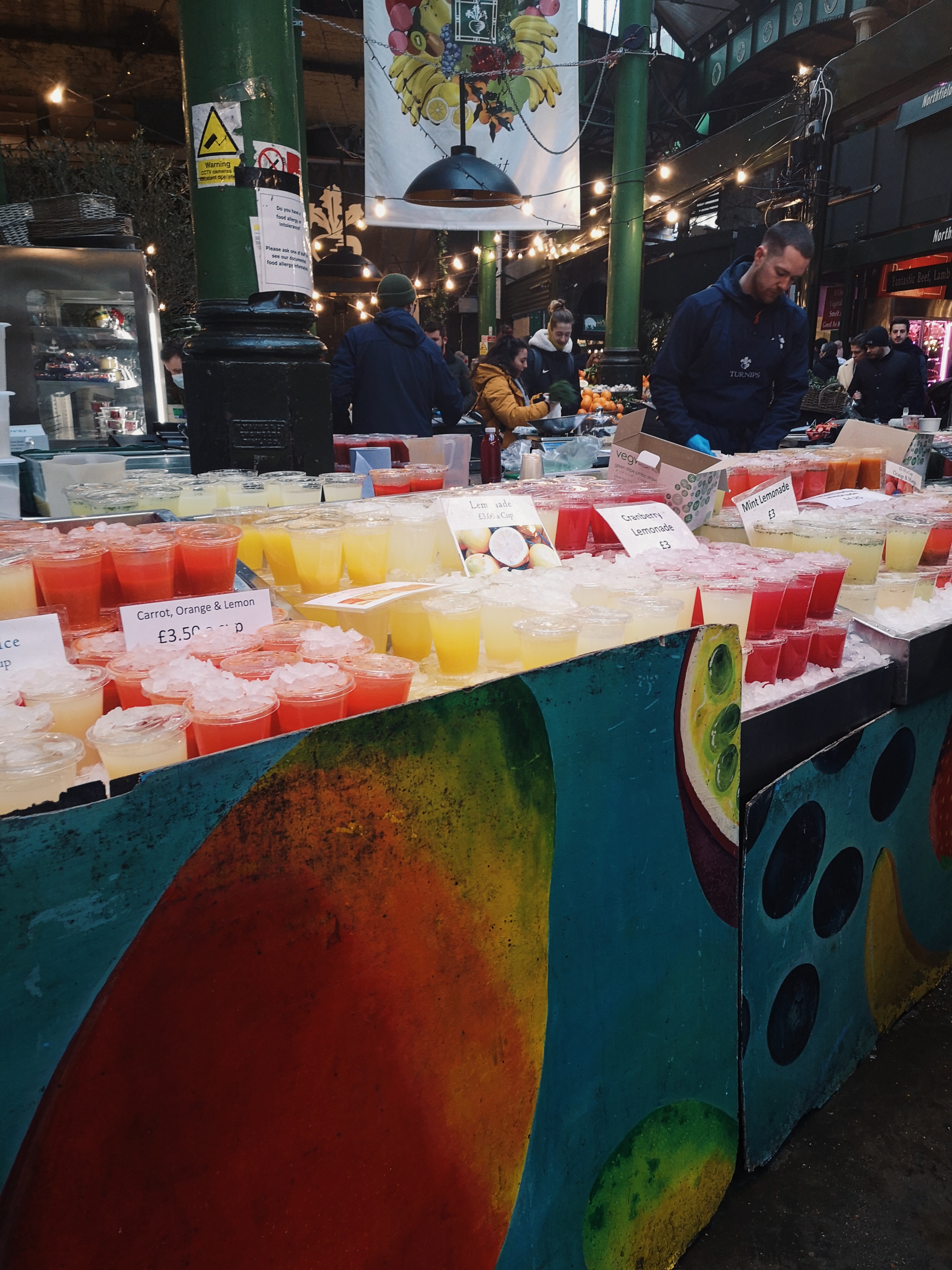 Various plastic cups filled with different colourful fruit juices lined up in trays of ice
