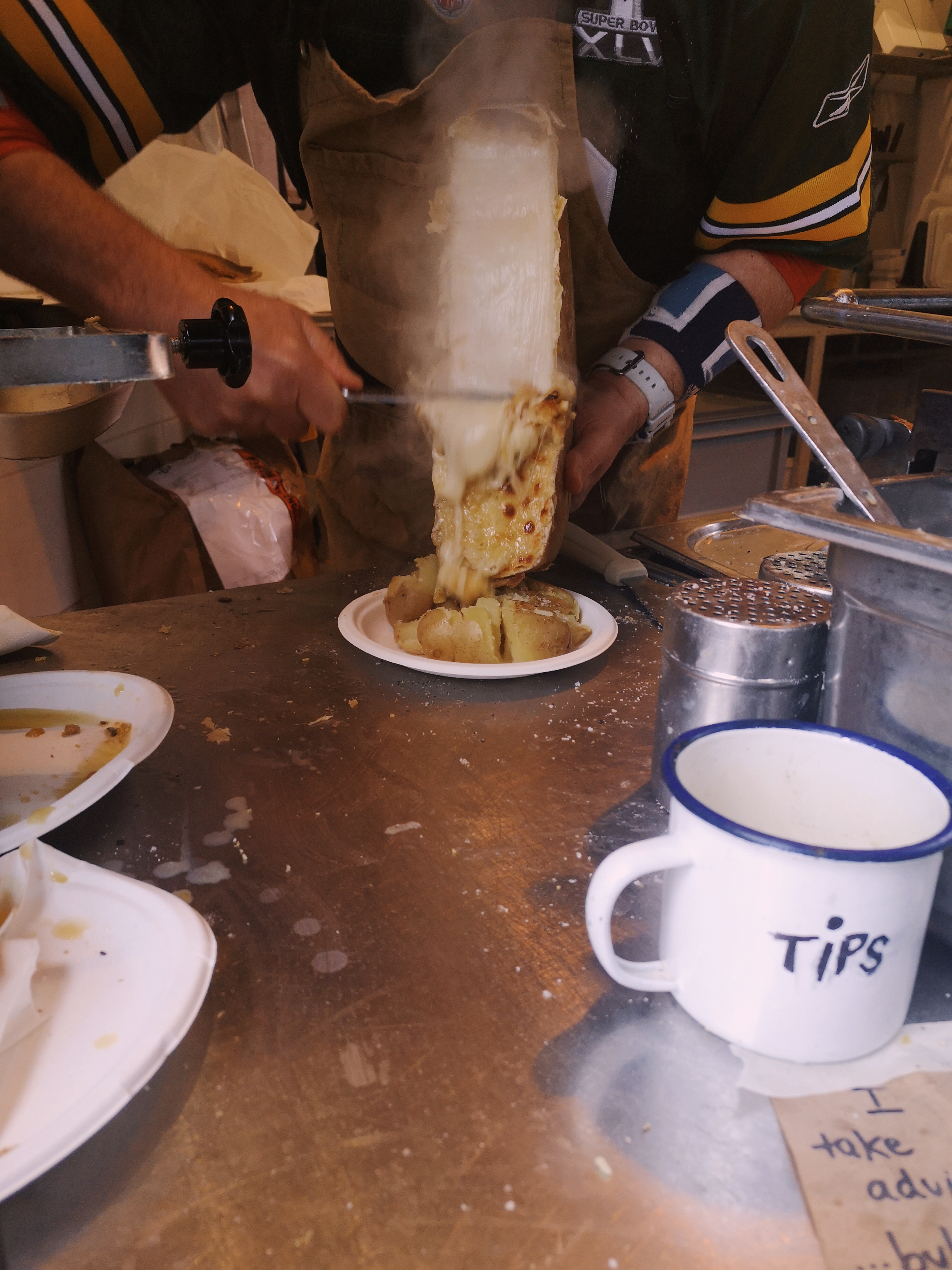 A guy scrapes the melted cheese off the block onto cooked potatoes