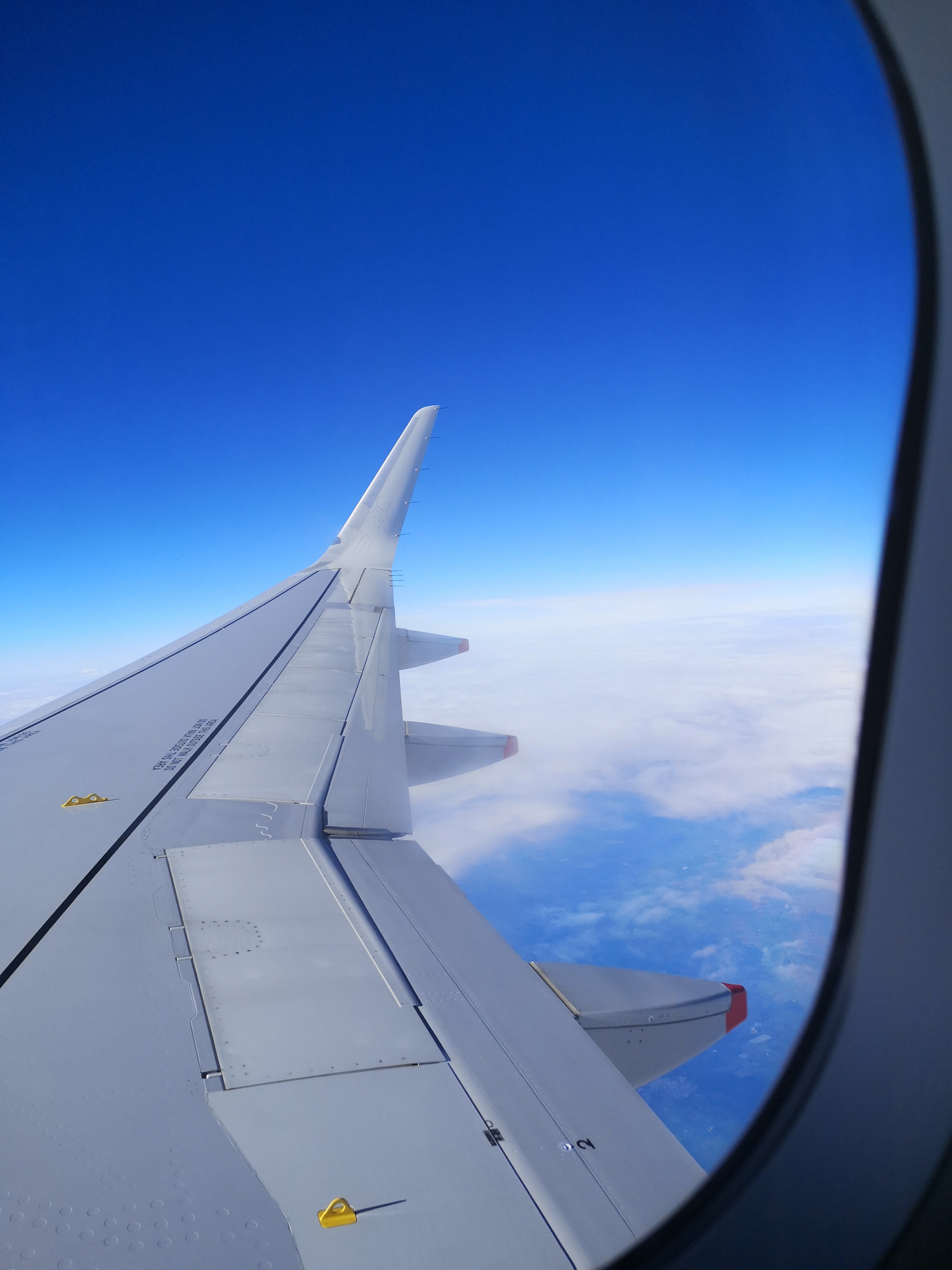 Looking out an airplane window with a blue sky and the plane wing floating over the cloud