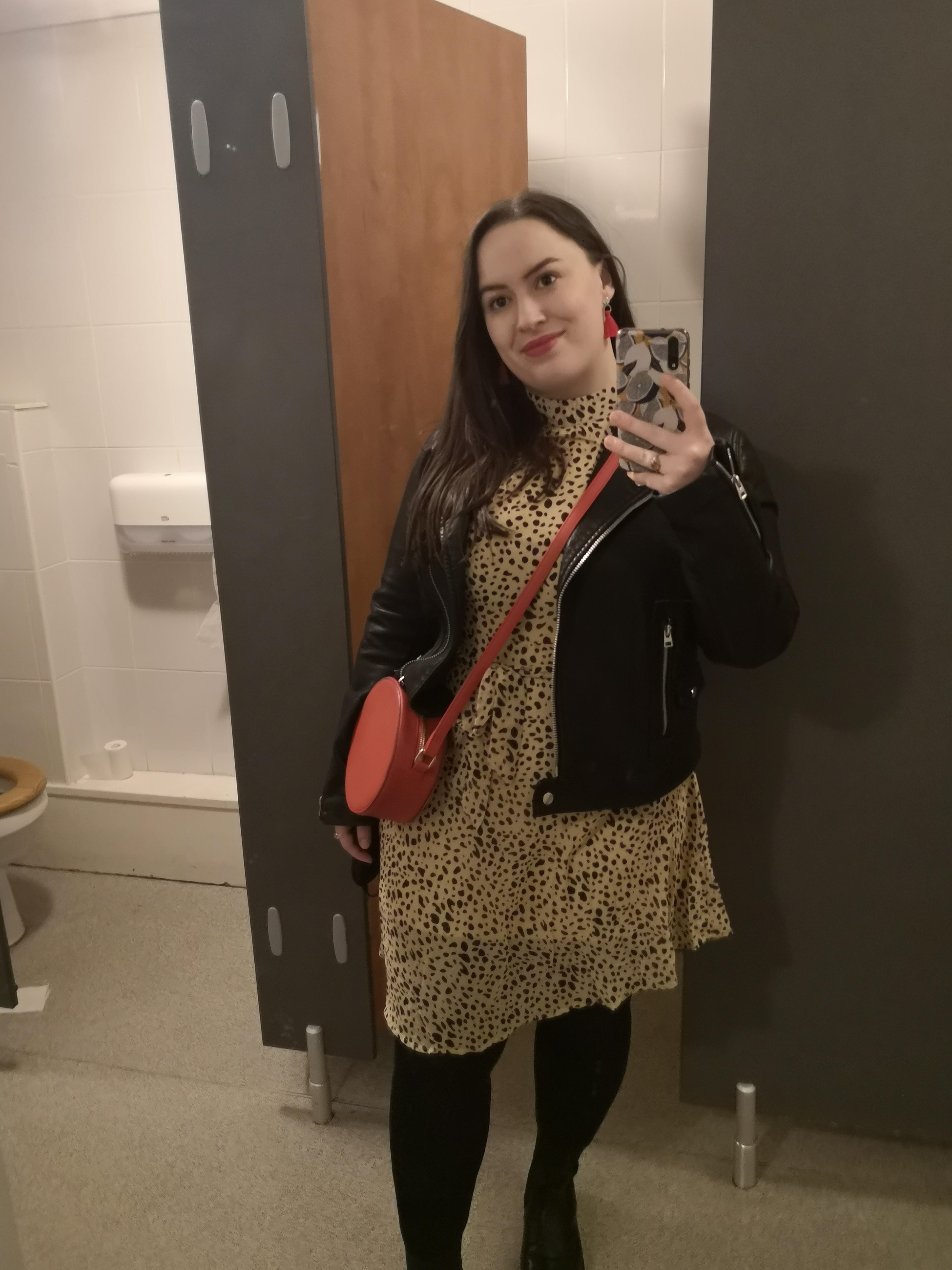 Me a short dark haired woman taking a photo in the mirror, I'm wearing a leopard print dress, black leather jacket and a red circuar bag
