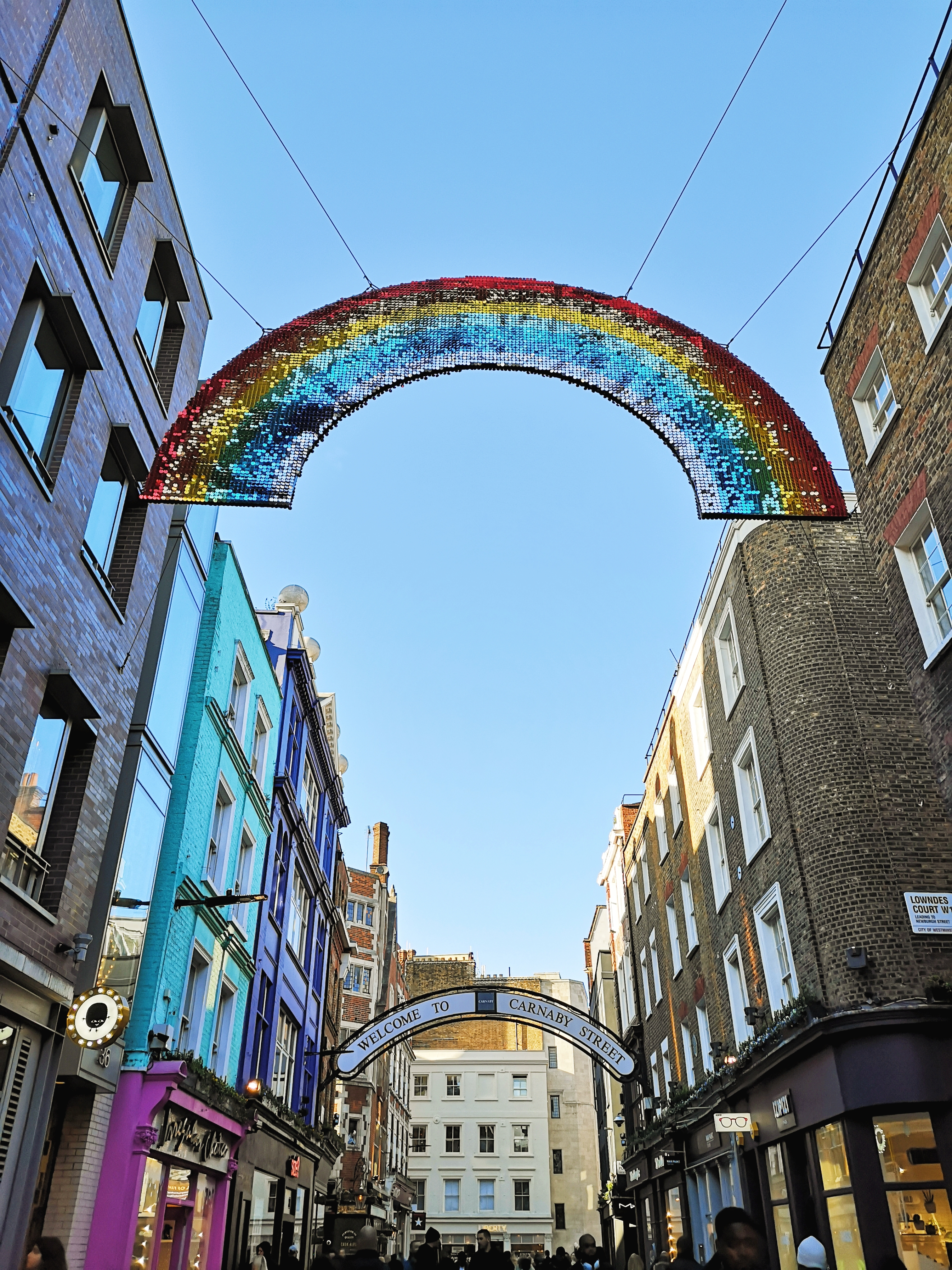 A glittery rainbow is strung up over Carnaby street with colourful buildings and shops