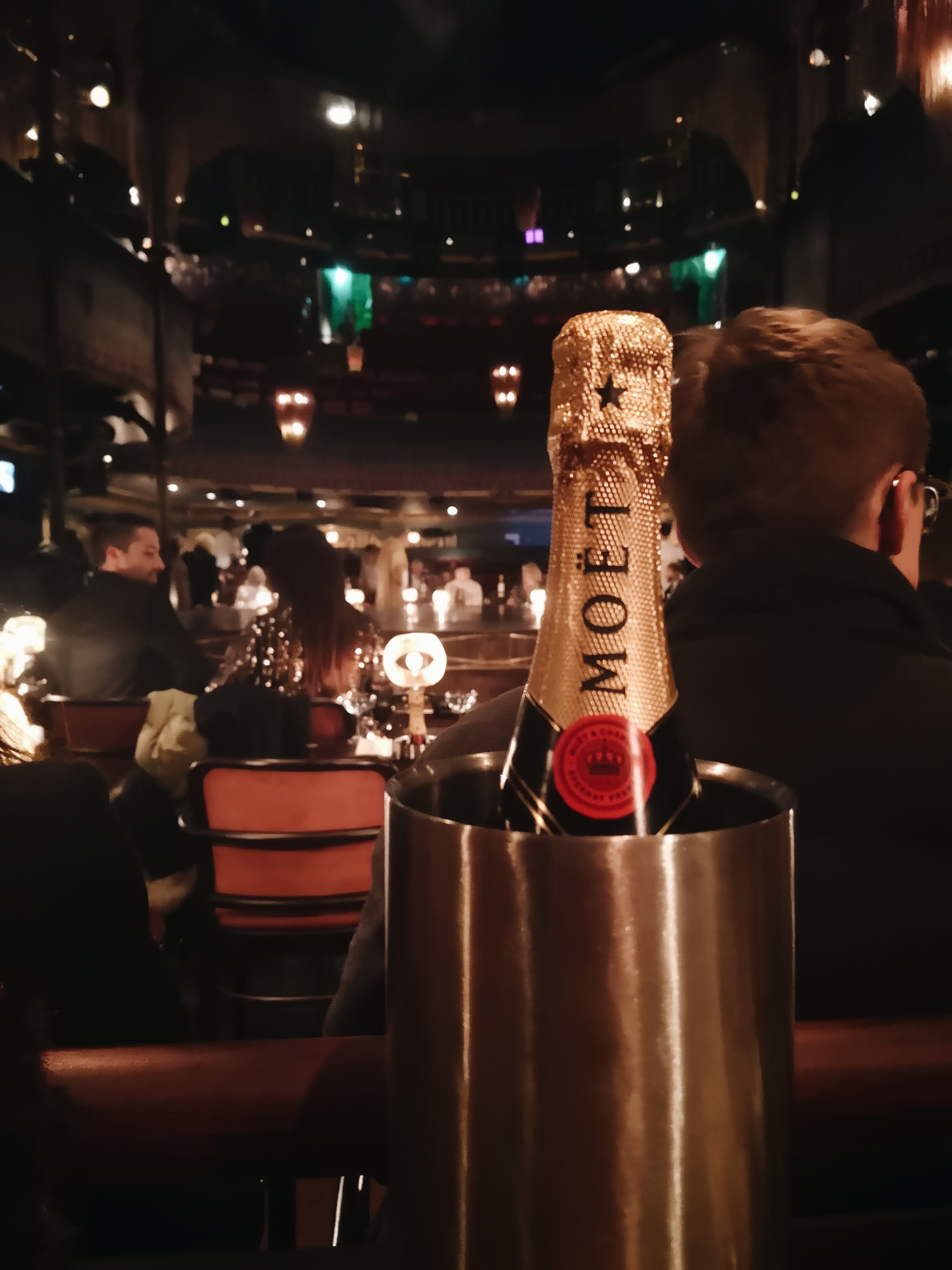 A bottle of Moet champagne sits in an ice bucket, balconies and the stage can be seen behind