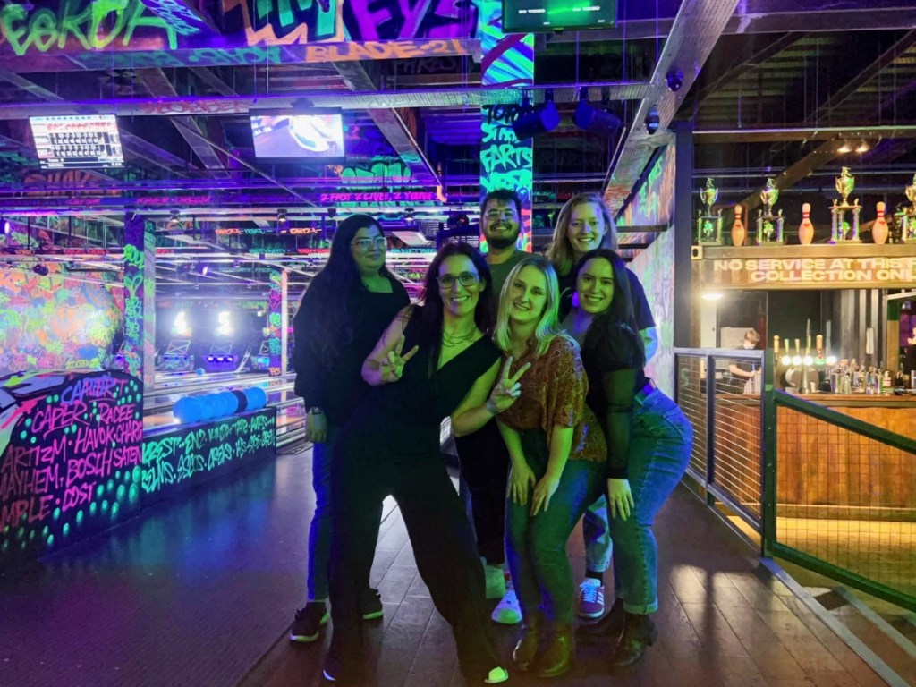 Six friends pose in front of a neon graffiti bowling alley