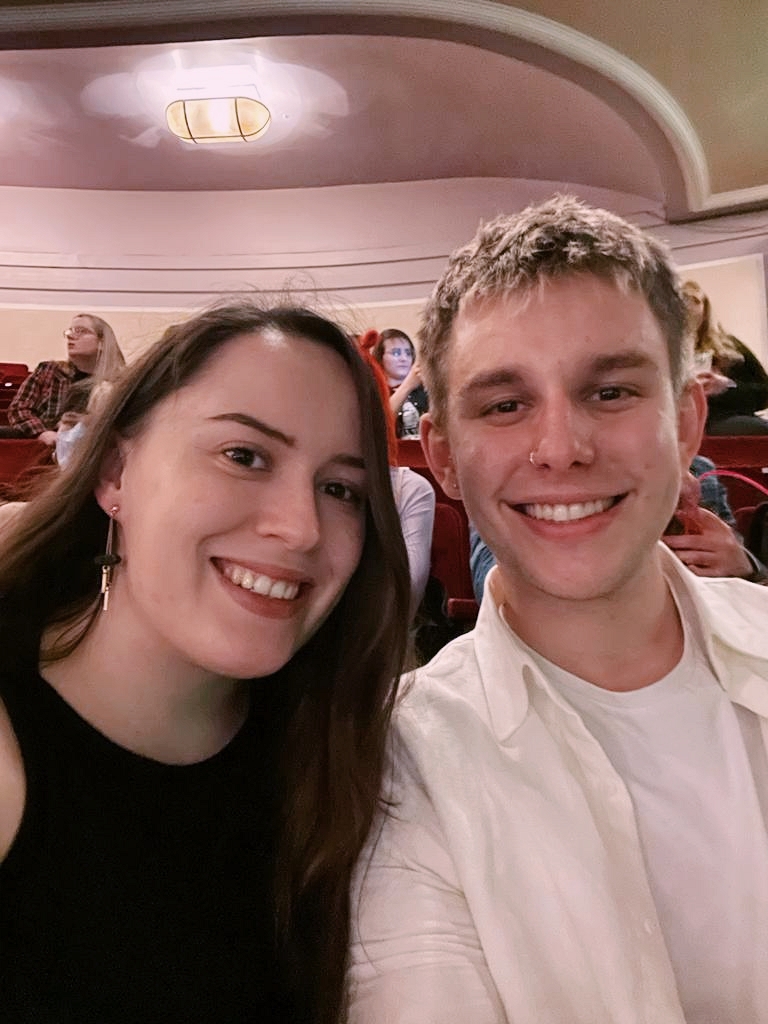 A selfie of my friend Ethan and I, we are both smiling 
I have a black top and long dark brown hair, he is wearing a white tshirt and shirt and has blonde hair