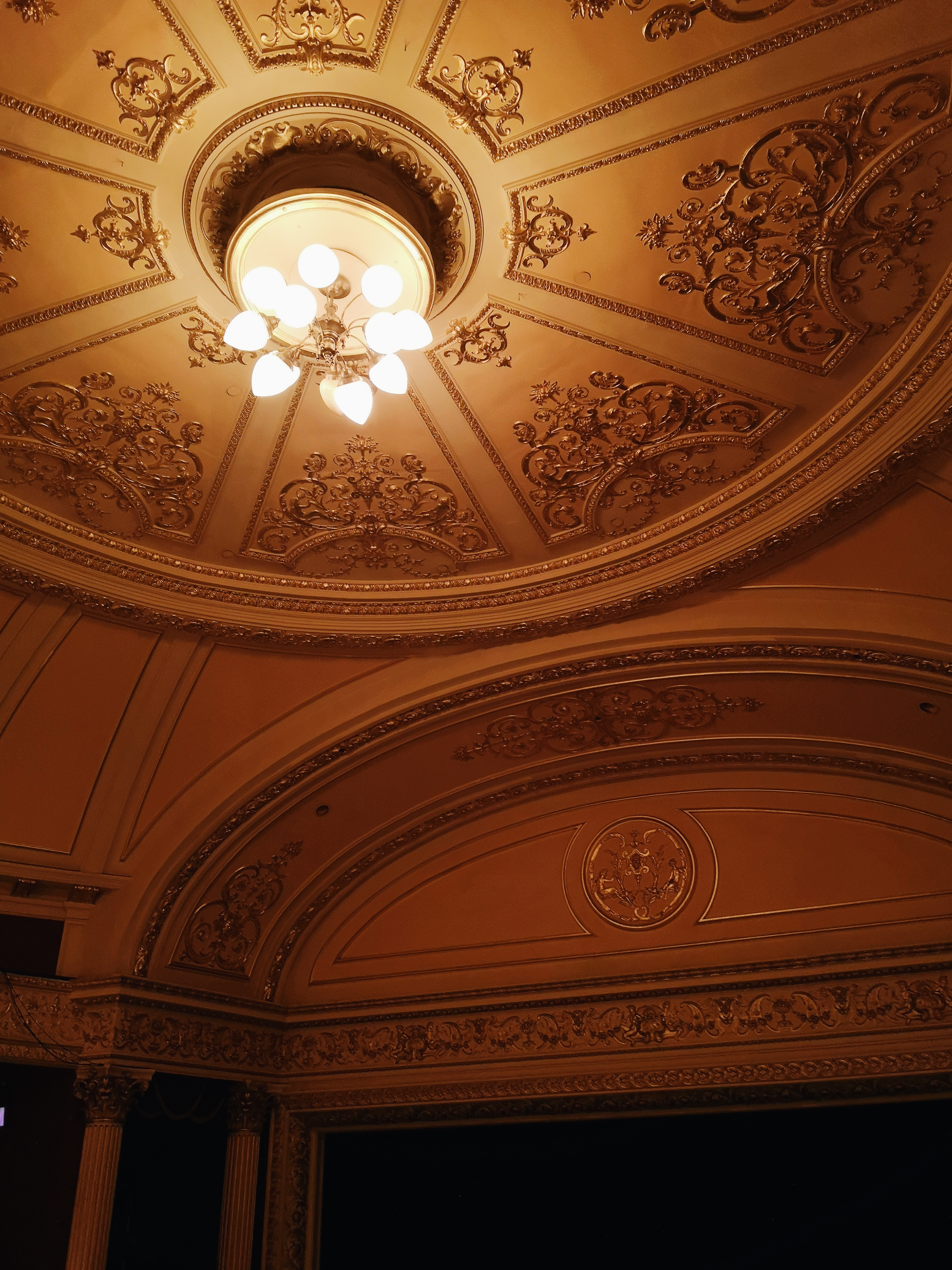 The ceiling of the Theatre Royal, cream with gold ornate trimmings and a small light in the centre