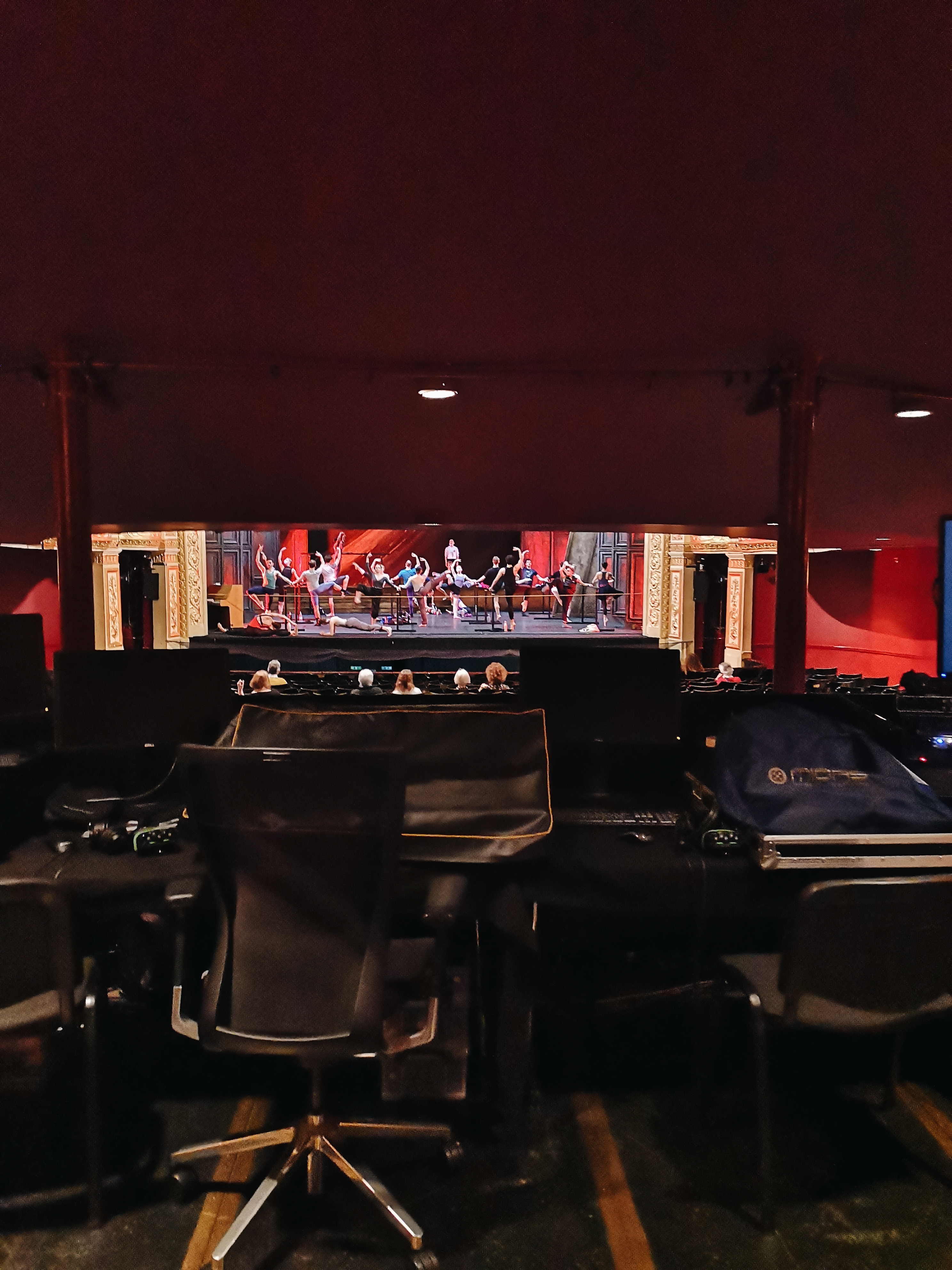 From the back of the stalls we can see a section of the stage where a company of ballet dancers are taking class at the barre