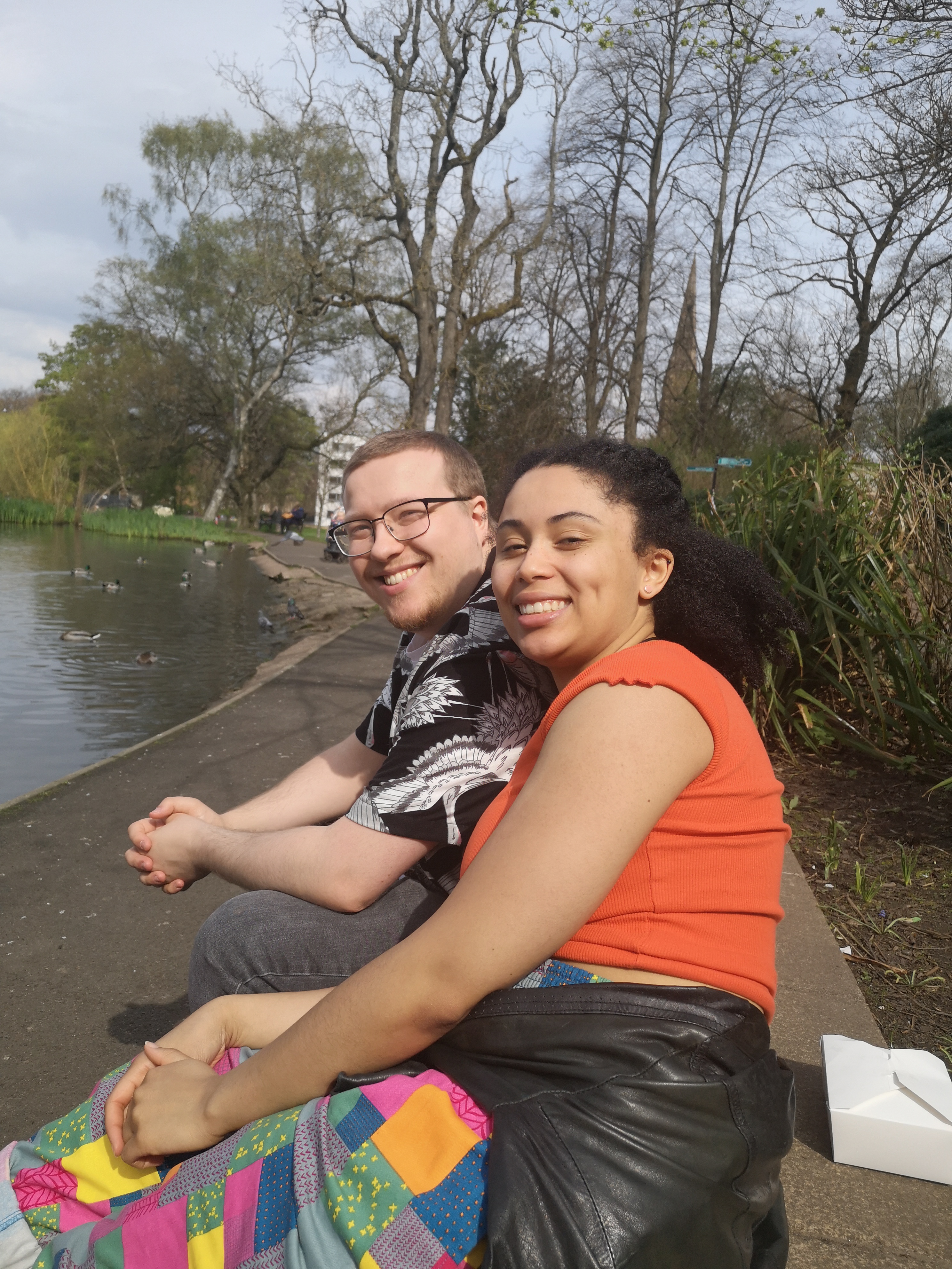 Two of my friends smile as they sit next to the duck pond in the park