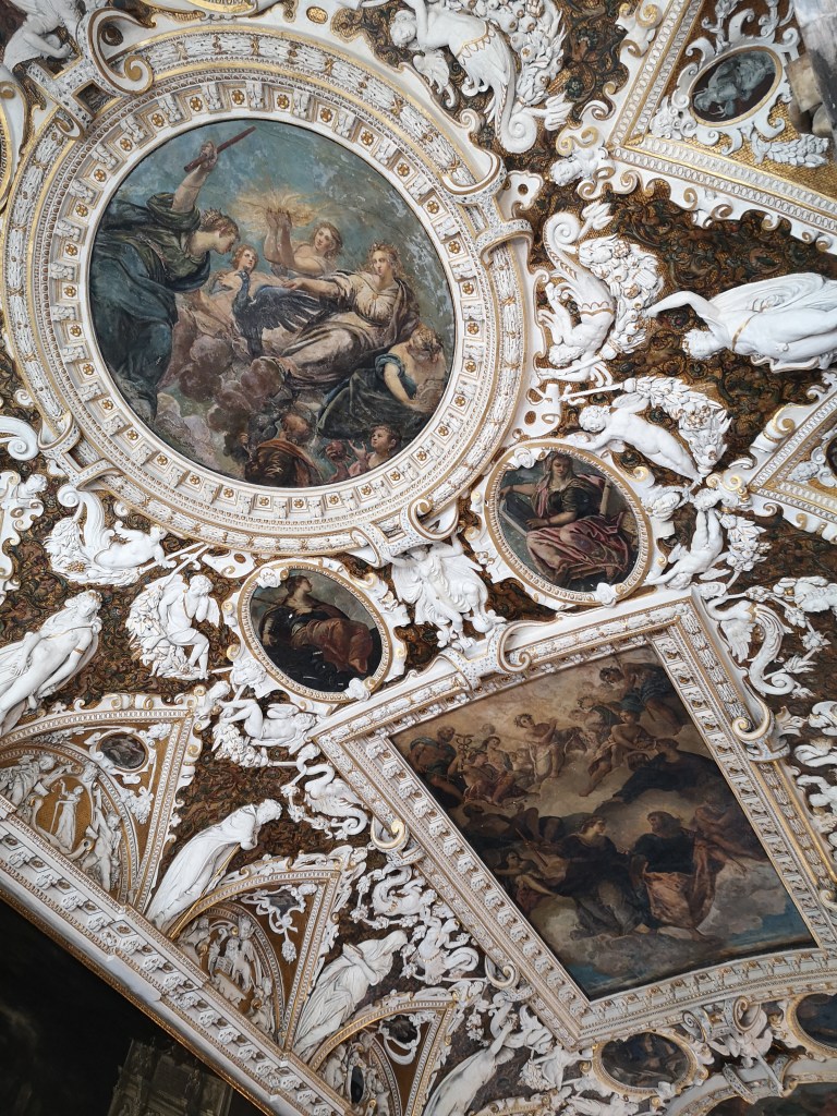 An ornate roof with old paintings and white and gold detailing