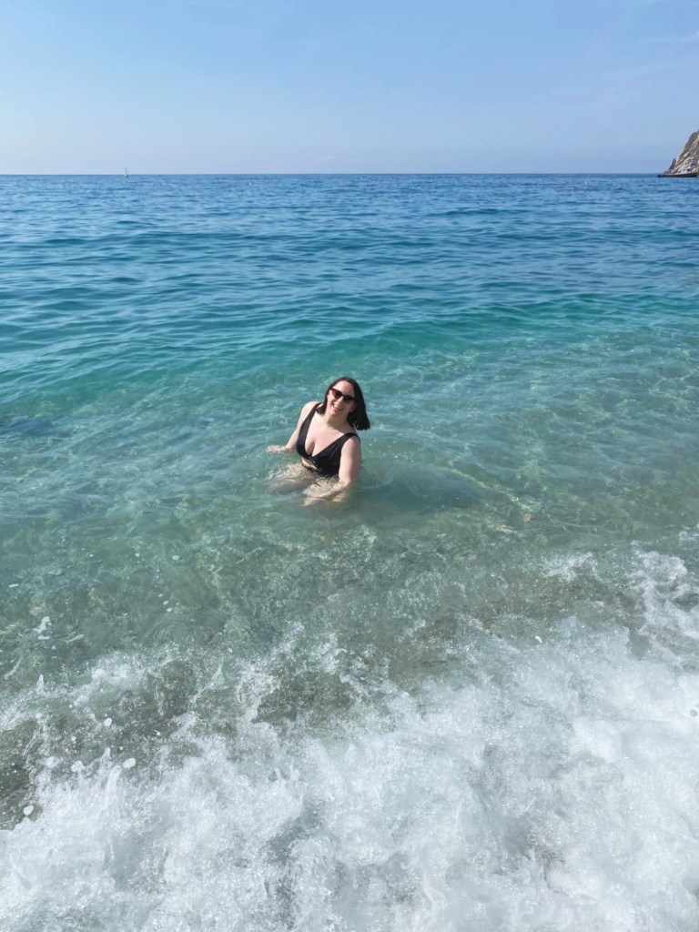 Lil katie sitting down in the blue sea with sunglasses on, smiling
