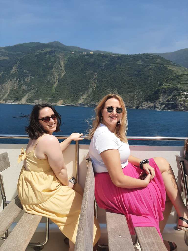 Katie and Hanna sit on a boat and smile toward Laura taking the picture