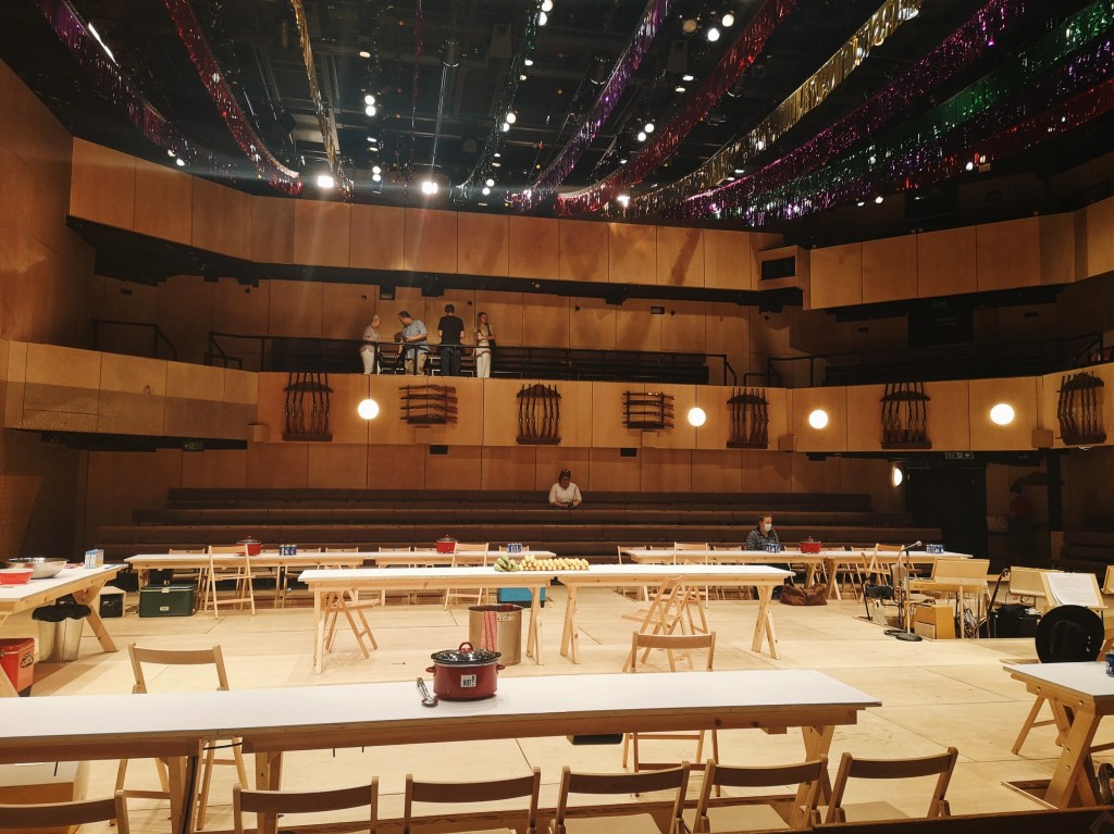 The stage of Oklahoma is a rectangular room, the whole room is light coloured wood and on stage there are long tables and chairs ready for a group dinner