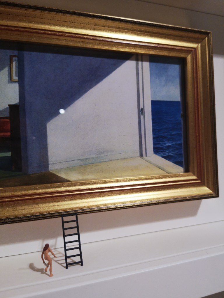 A tiny woman takes off her clothes as she moves toward the tiny ladder that leads up to a painting showing the sea