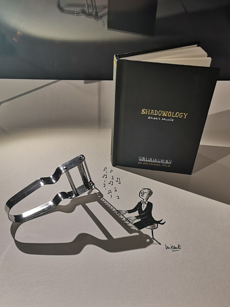 An art piece where the shadow of a vegetable peeler is turned into a man playing the piano by the artist drawing in the rest of the details