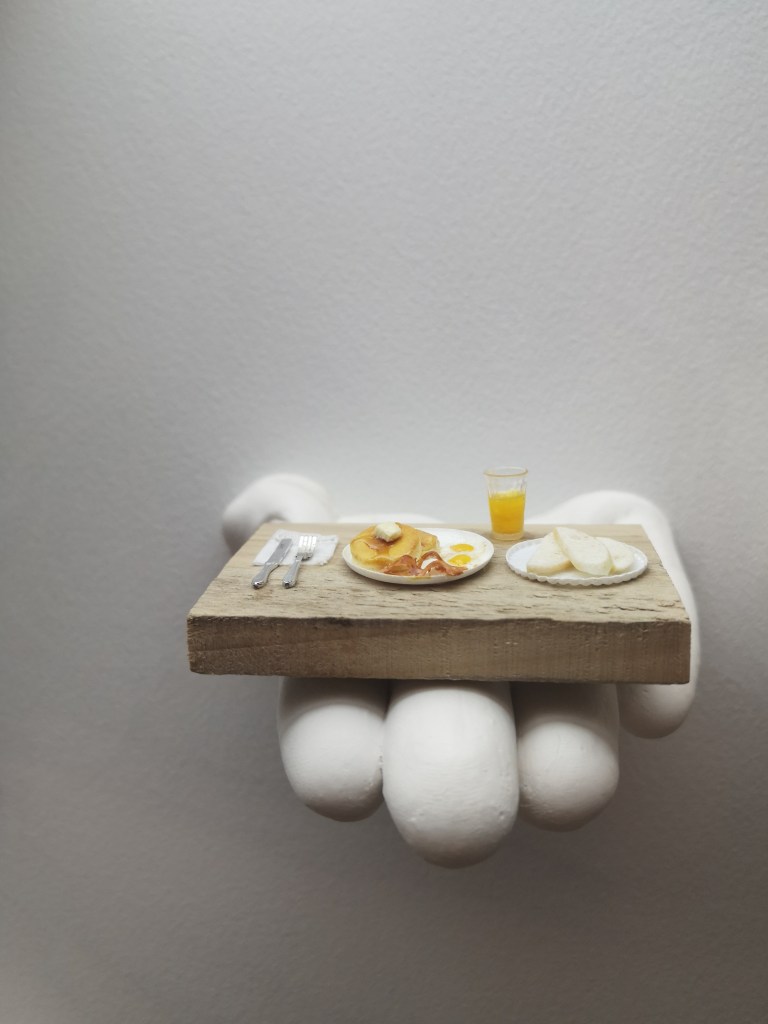A very tiny pancake breakfast on a hand sticking out from the wall
