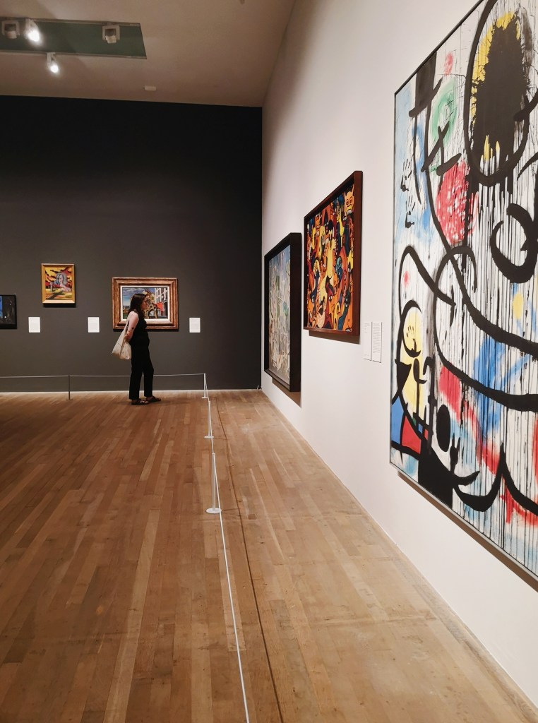 In a gallery full of colourful paintings my sister stands looking at one