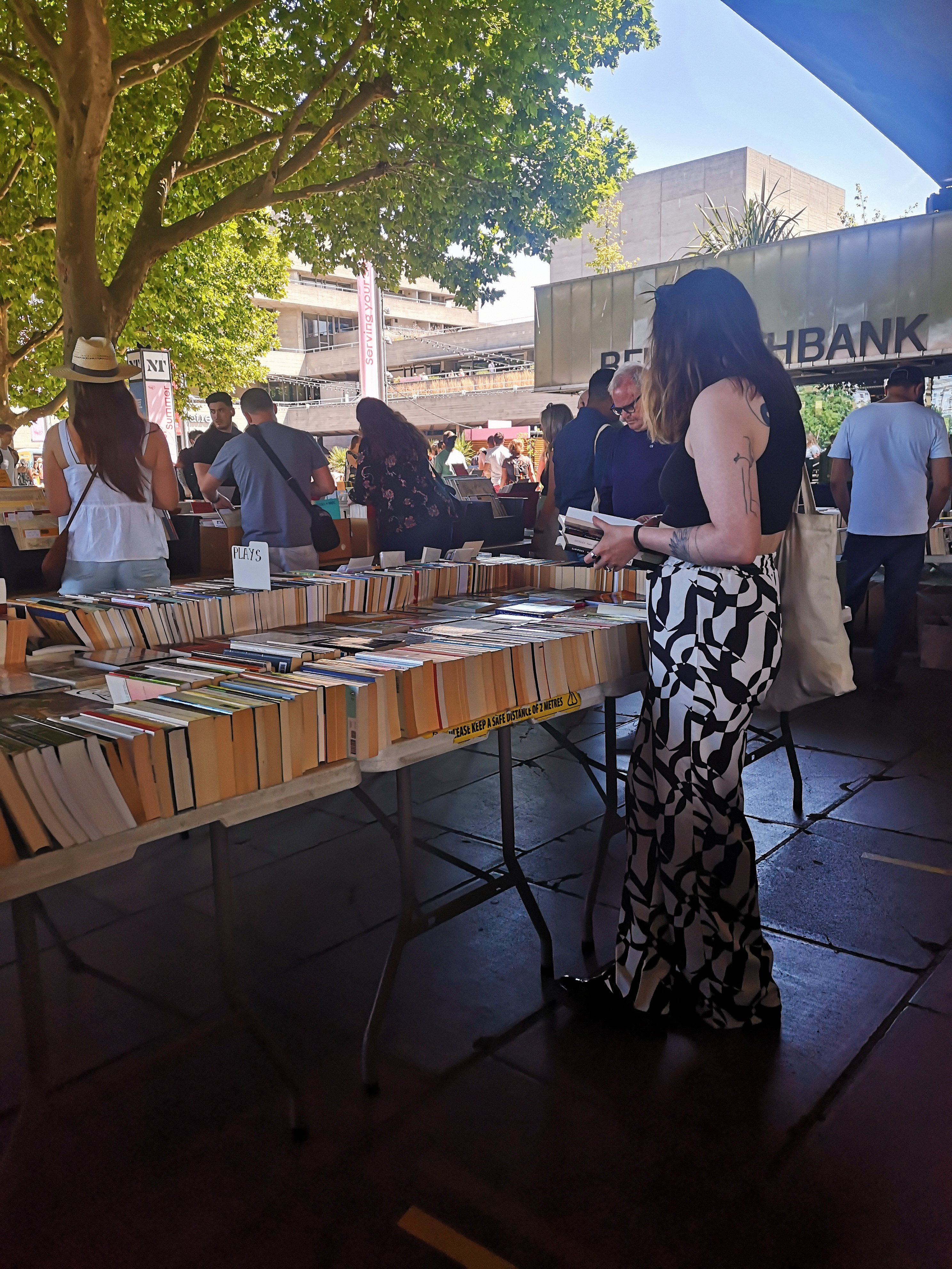 A gal stands with books in her hands browsing the table full of other books