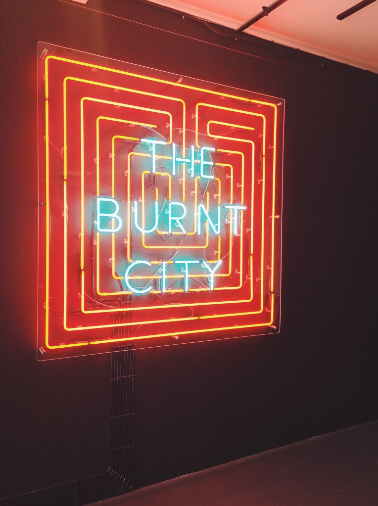 A neon sign representing a labyrinth with the words The Burnt City on it