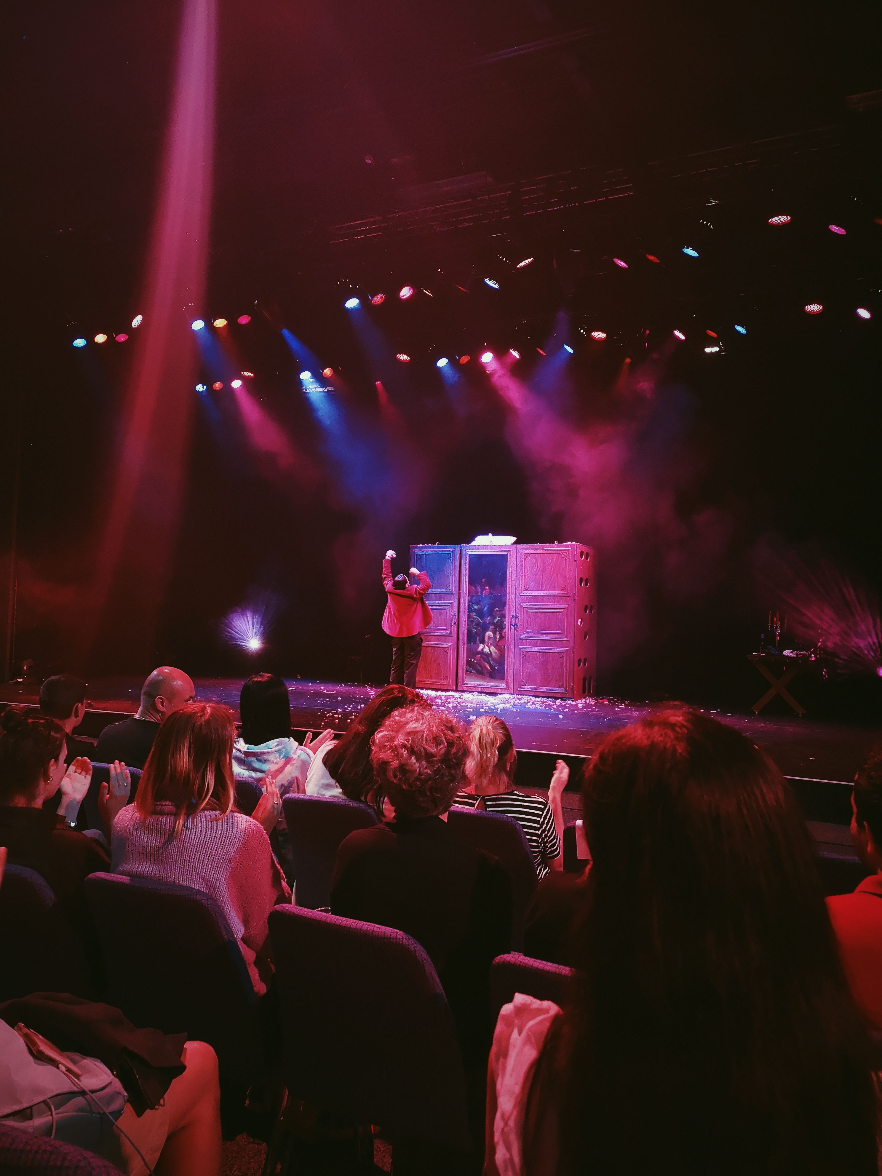 Under red and blue beams of light a man dances, punching his fists over his head