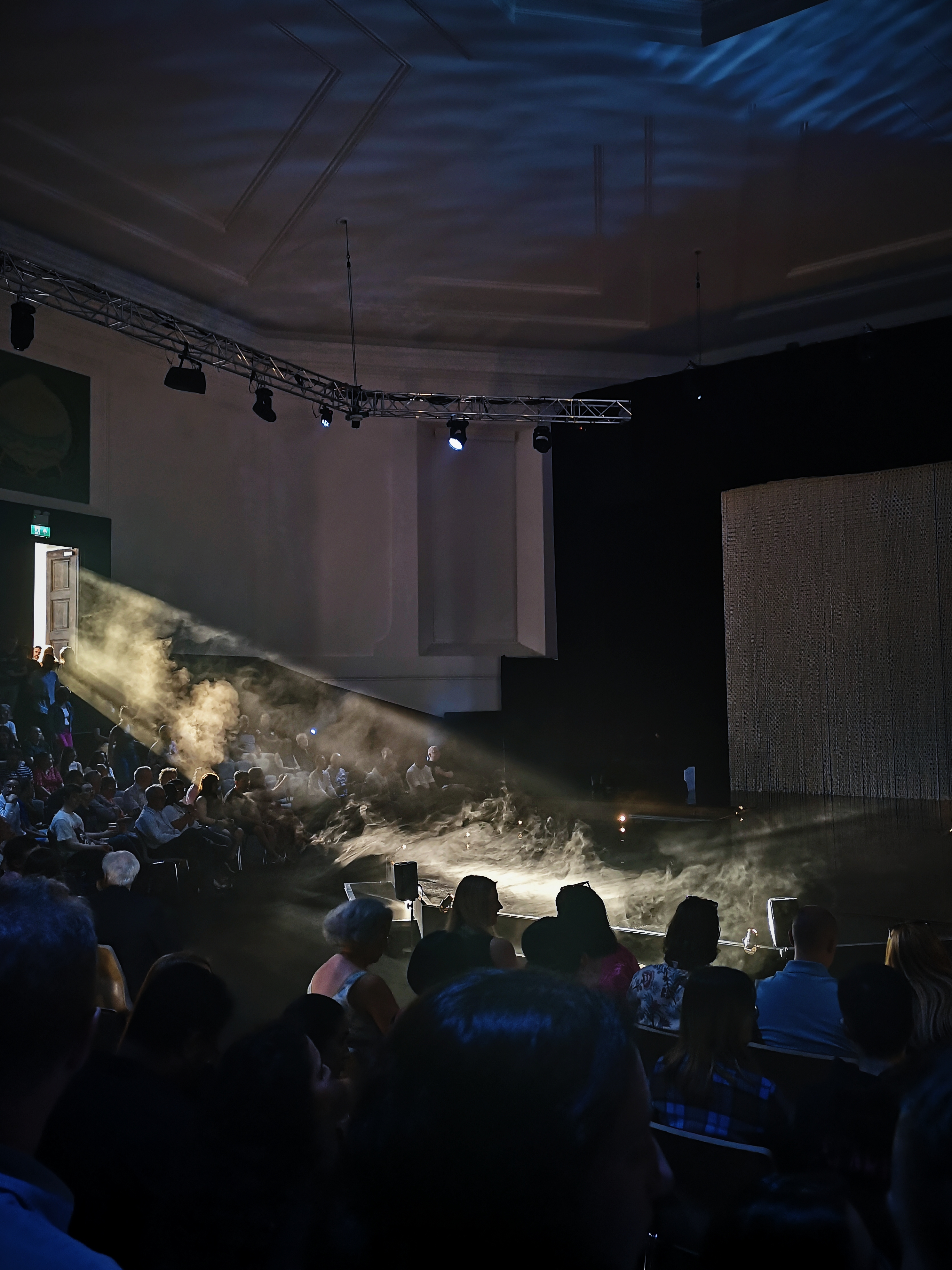 In a dark room, light pours in from a door illuminating smoke in the air