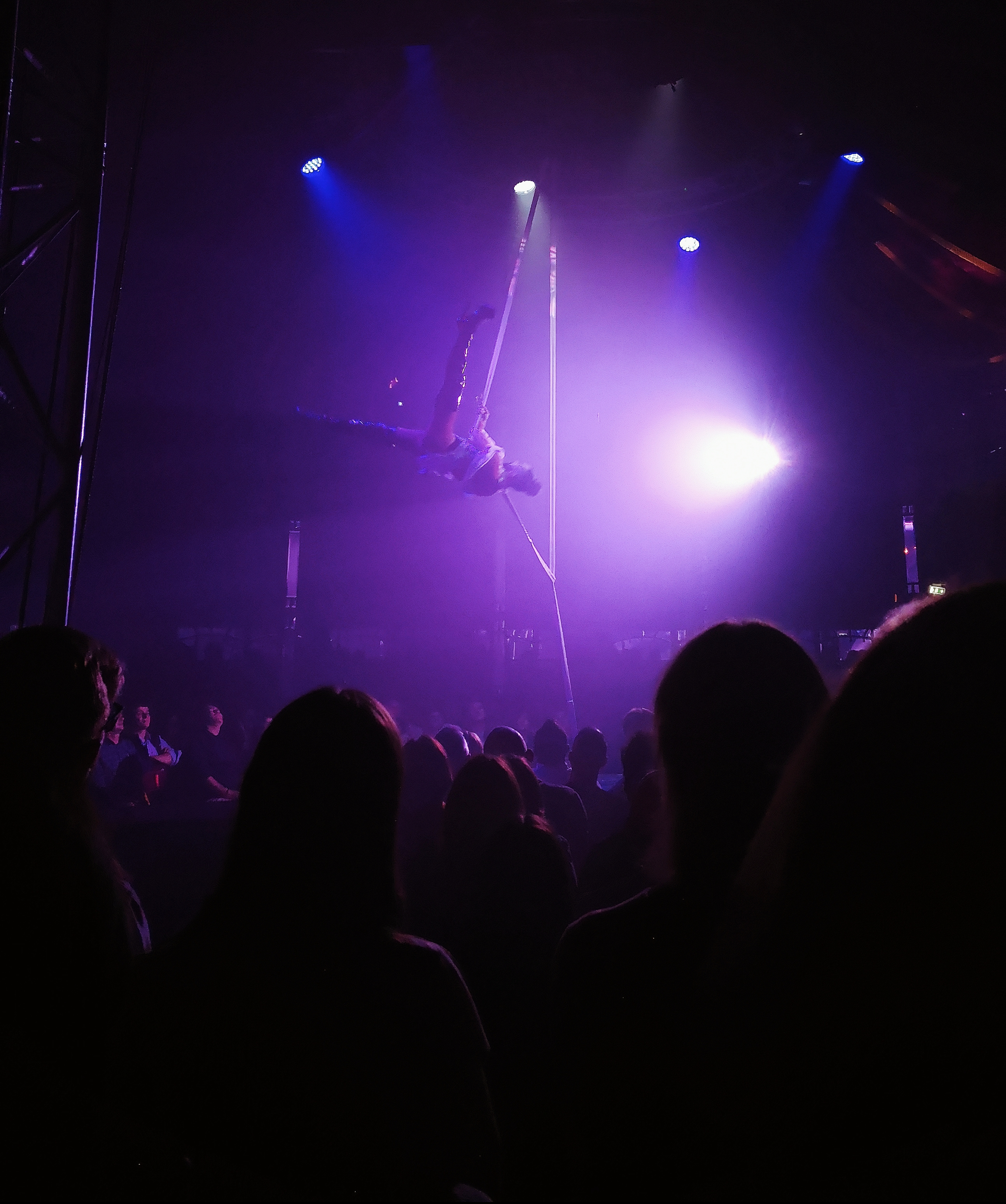 A person in thigh high black heels spreads their legs while swinging in the air on a rope hung from the ceiling