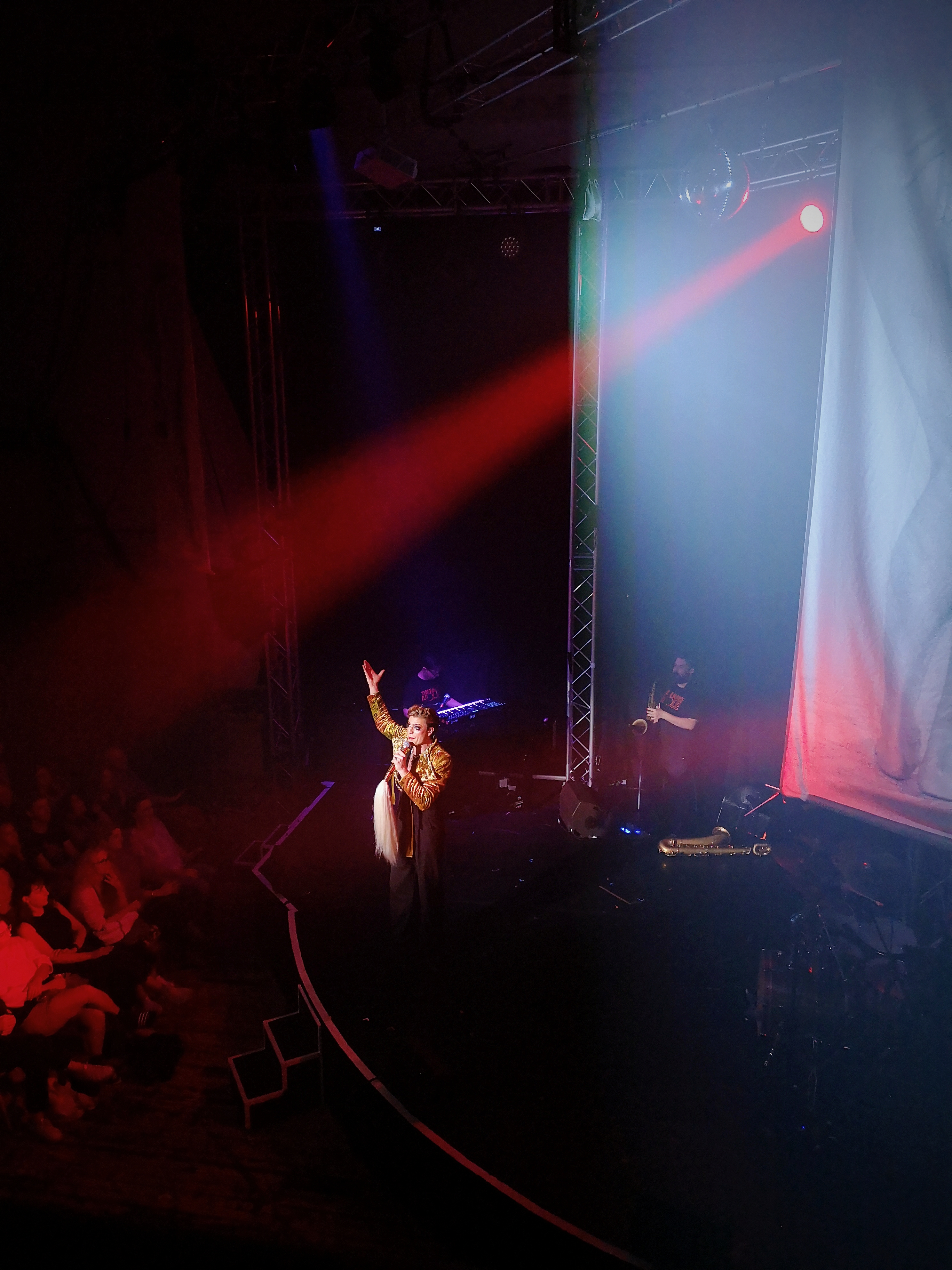 Reuben Kaye stands on stage singing into a microphone with one hand held in the air