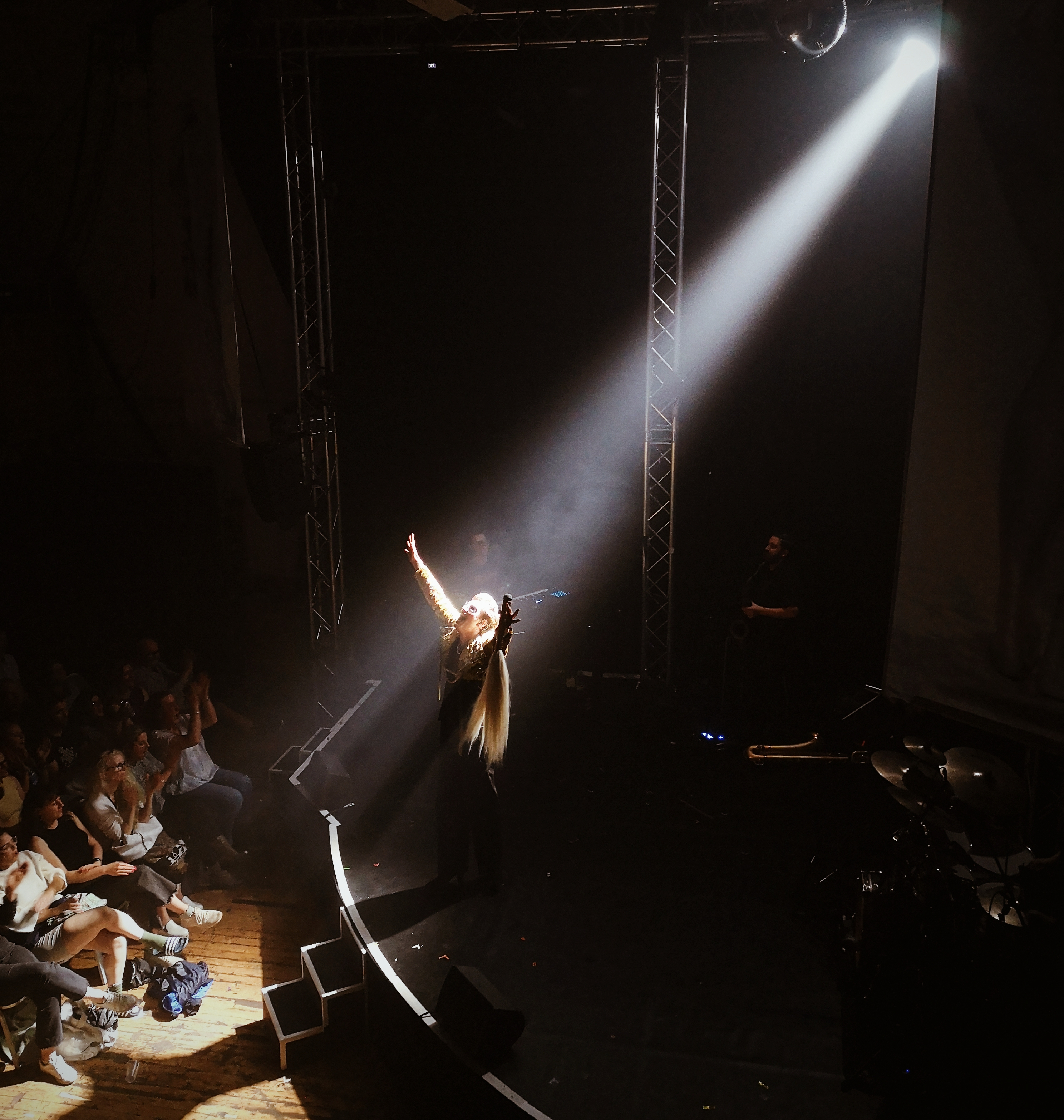 Reuben stands with his arms raised up, head back and eyes closed in a spotlight while people applaud