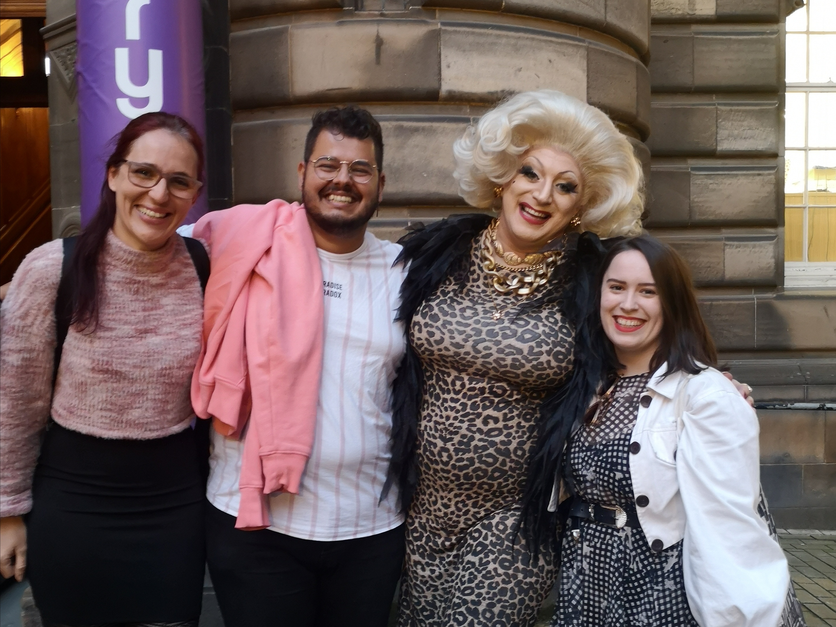 Three regular people (me and my friends) smile alongside famous drag queen Myra Dubois who is very funny