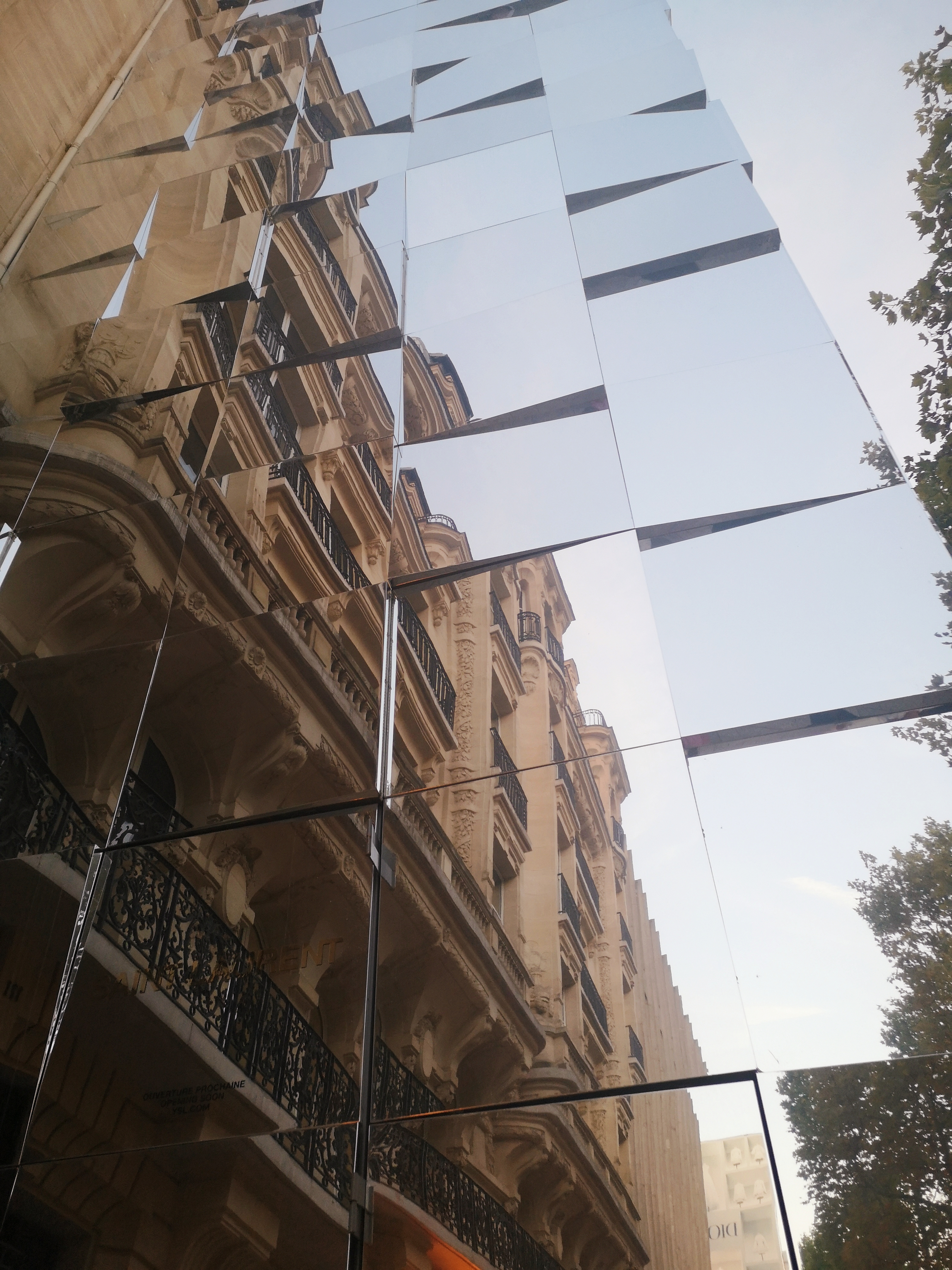 An uneven mirrored wall reflects a parisian building