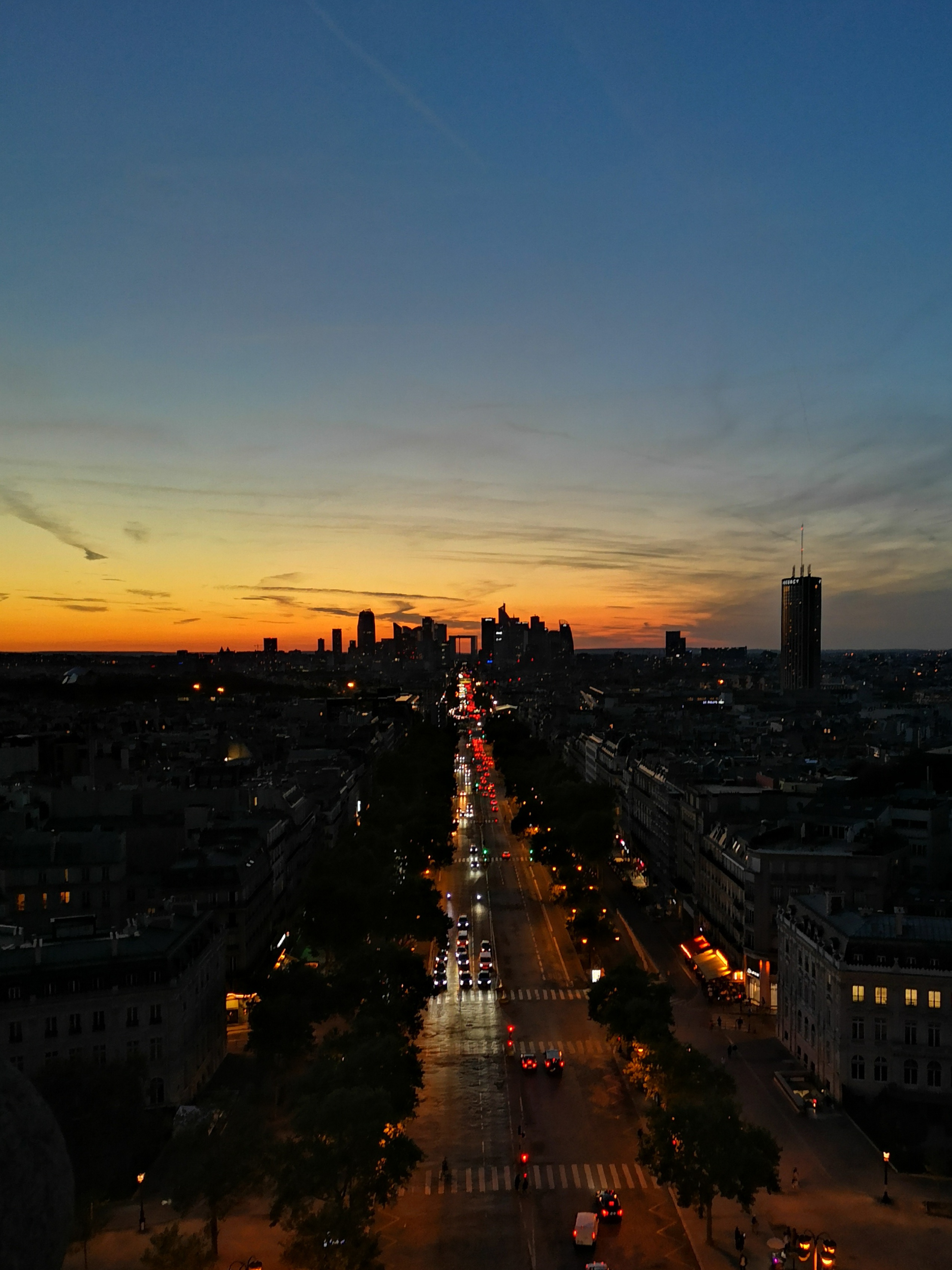 A grand avenue filled with car headlights, with the sunset shining in the sky