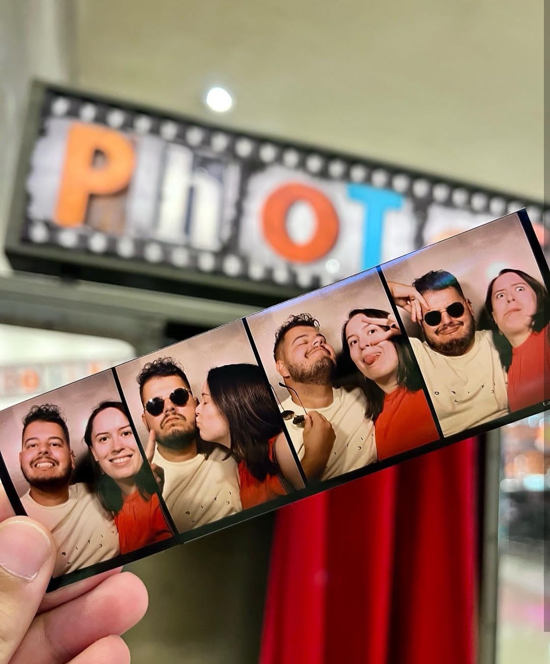 A hand holds up a strip of photo booth photos where Bruno and I make a variety of nice and stupid faces