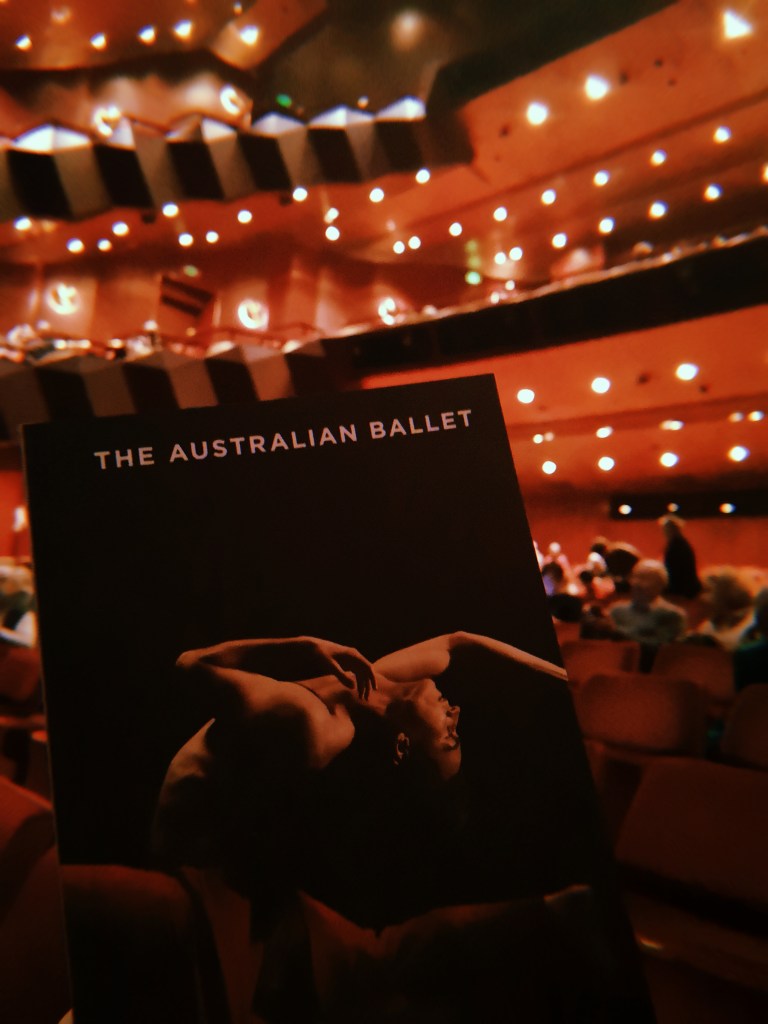 Holding up a programme for The Australian Ballet with the red theatre seats in the background