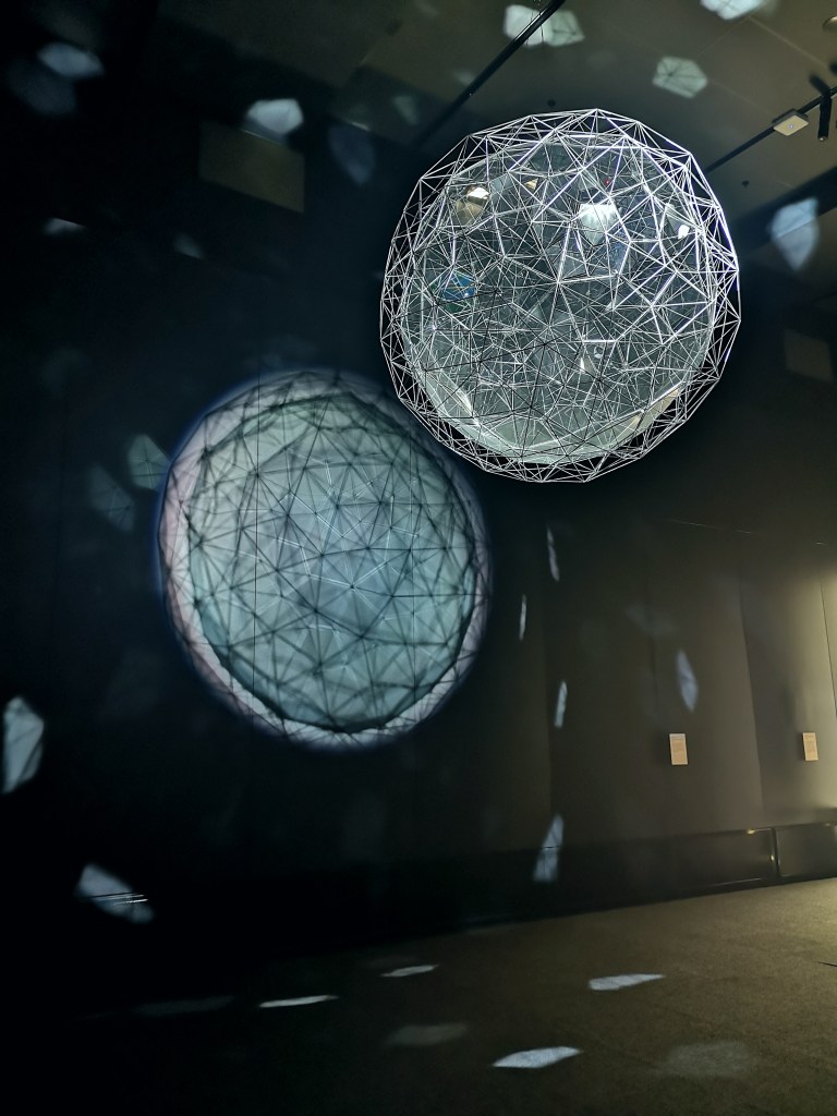 A glass and metal ball hangs from the ceiling, light shining through projects onto the wall behind